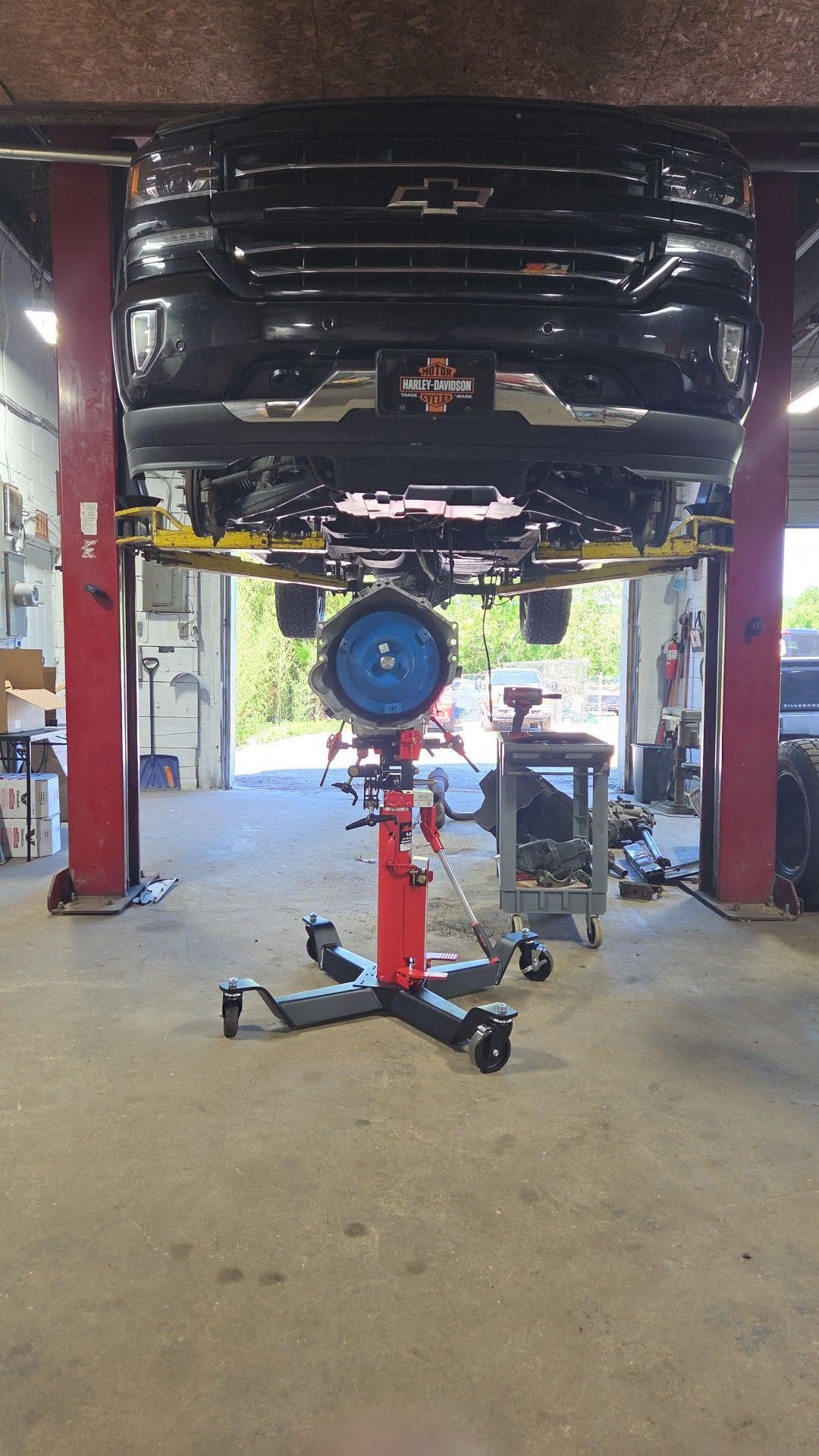 Black car lifted on a garage hoist with a blue wheel hub tool centered below it