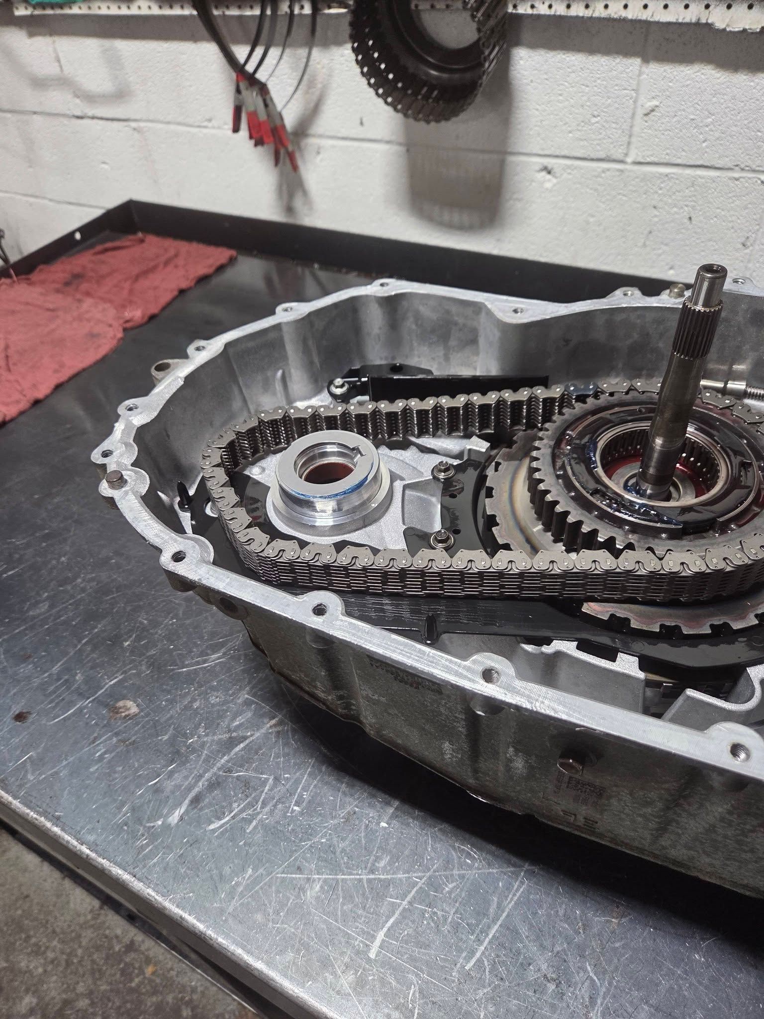 Open engine case with chain, gears, and a gasket on a metal workbench in a workshop