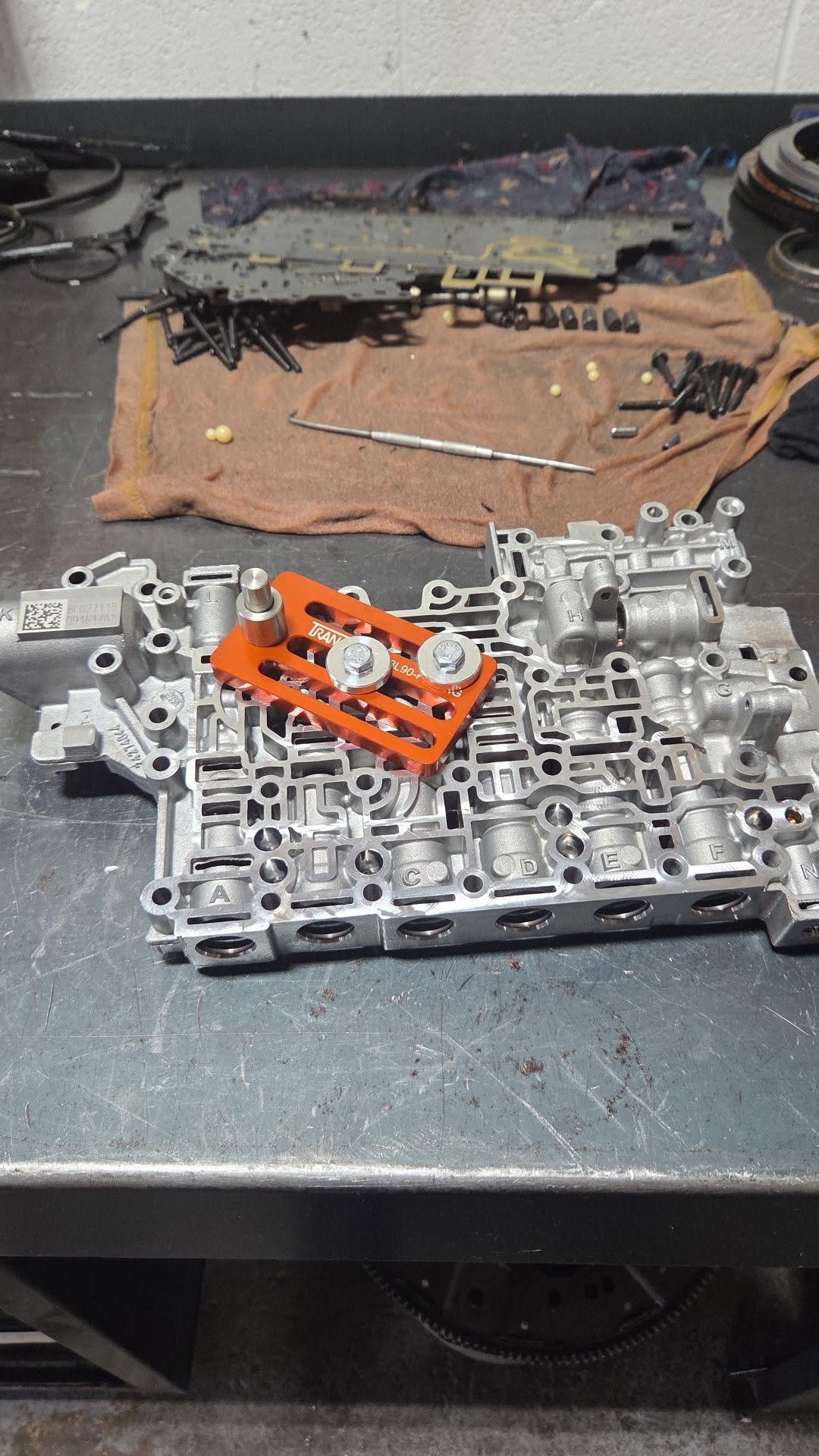 Disassembled car transmission parts laid out on a workbench, including metal housings, valves, and orange components