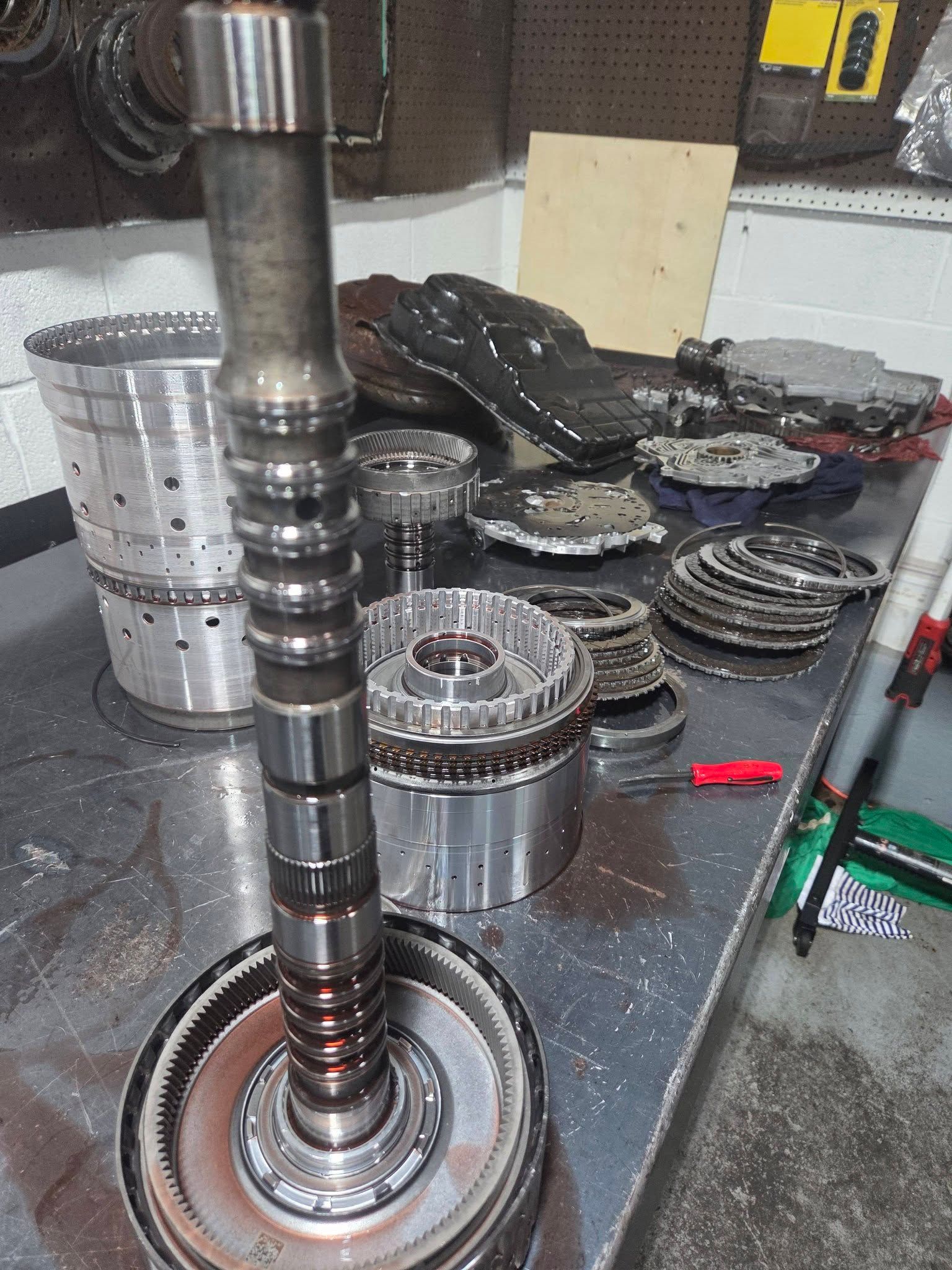 Disassembled metal transmission parts and shaft laid out on a workbench in a repair shop