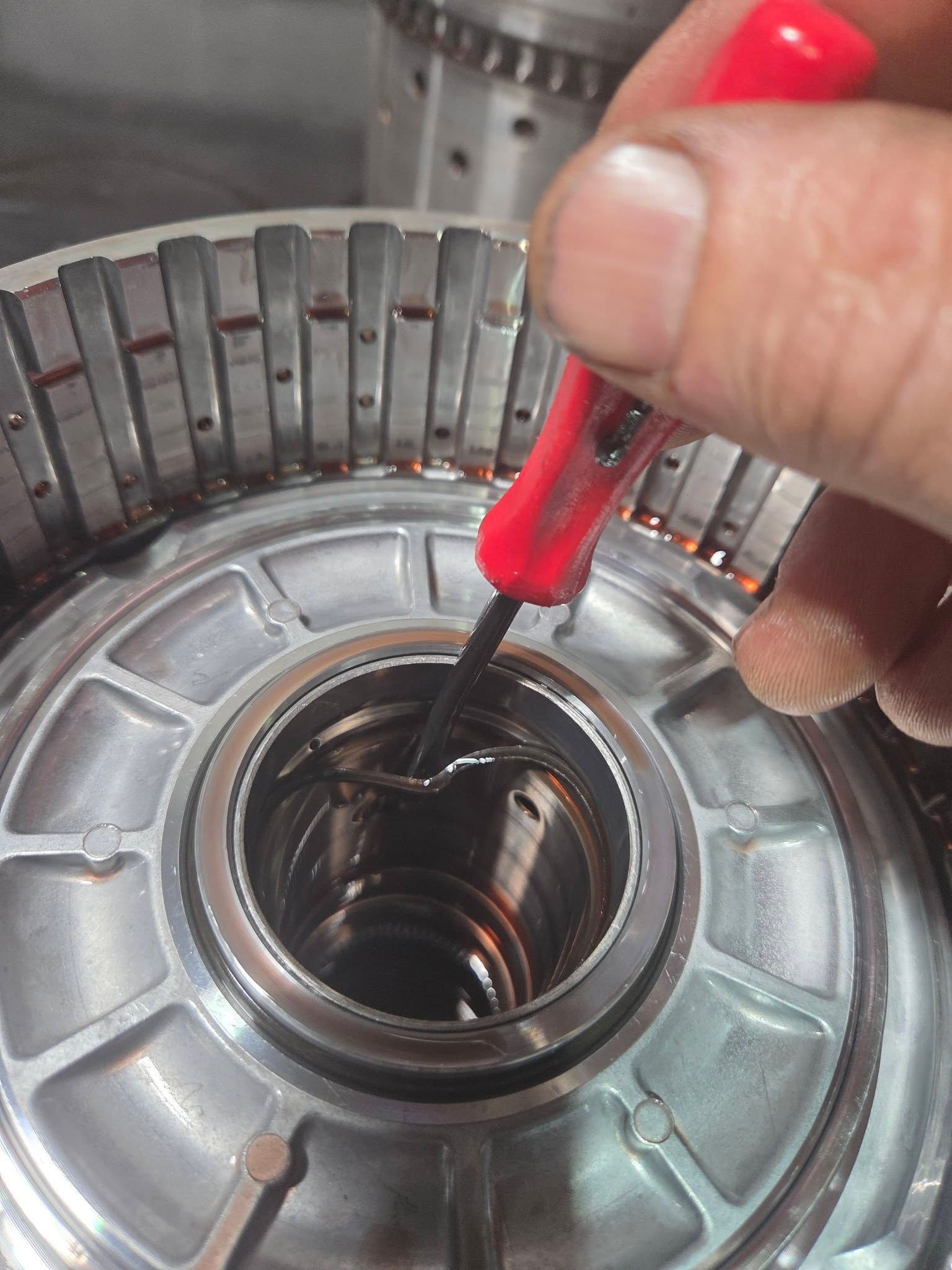 Close-up of a hand using a red screwdriver to adjust a metal appliance part.