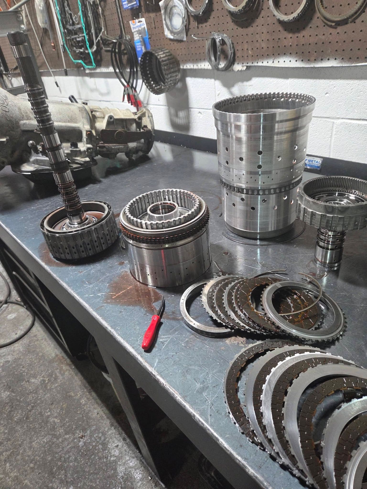 Disassembled metal transmission parts on a workbench in a mechanic’s shop.