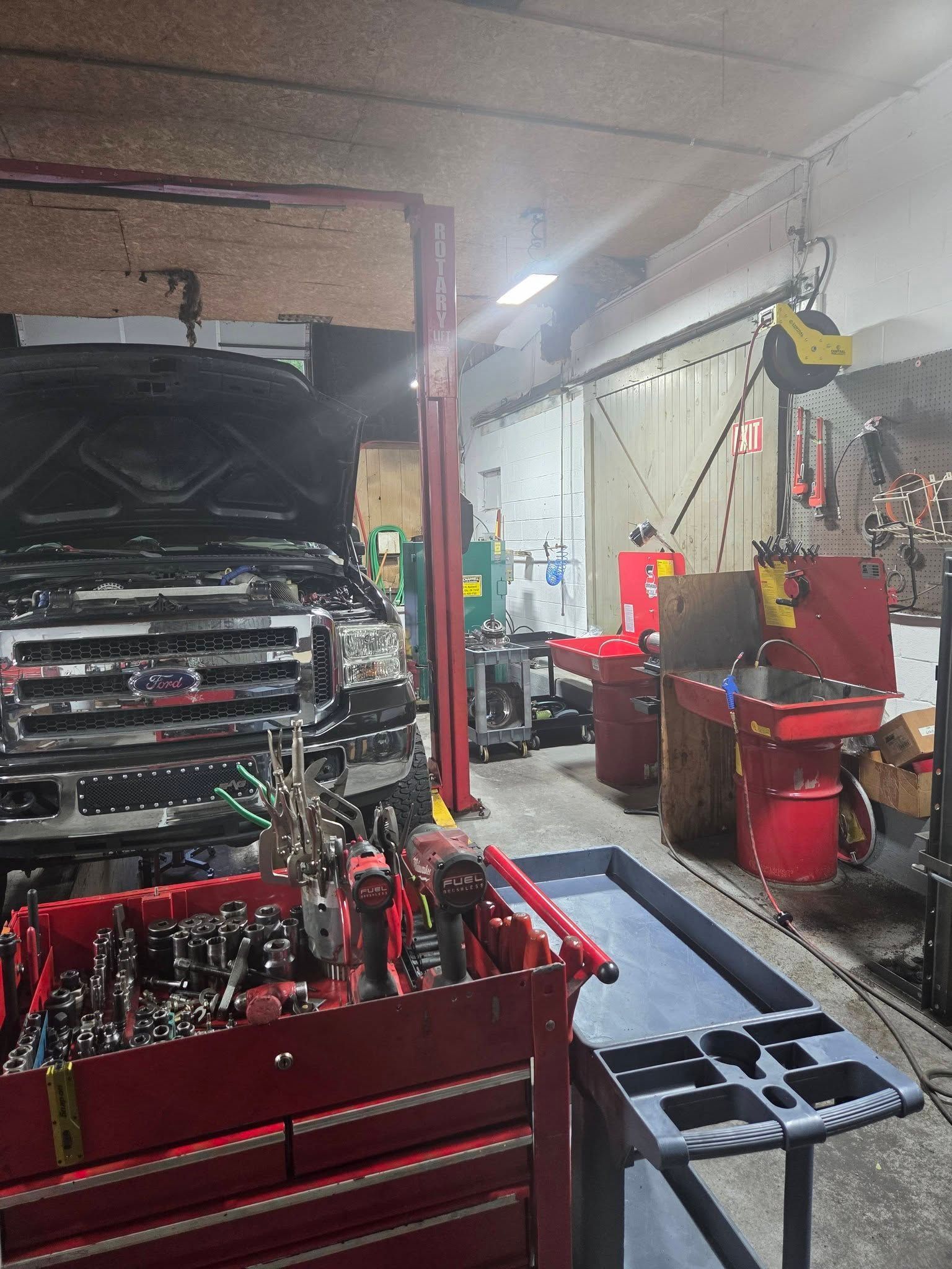 Auto repair shop with a car on a lift, red tool carts, and scattered tools in a cluttered garage