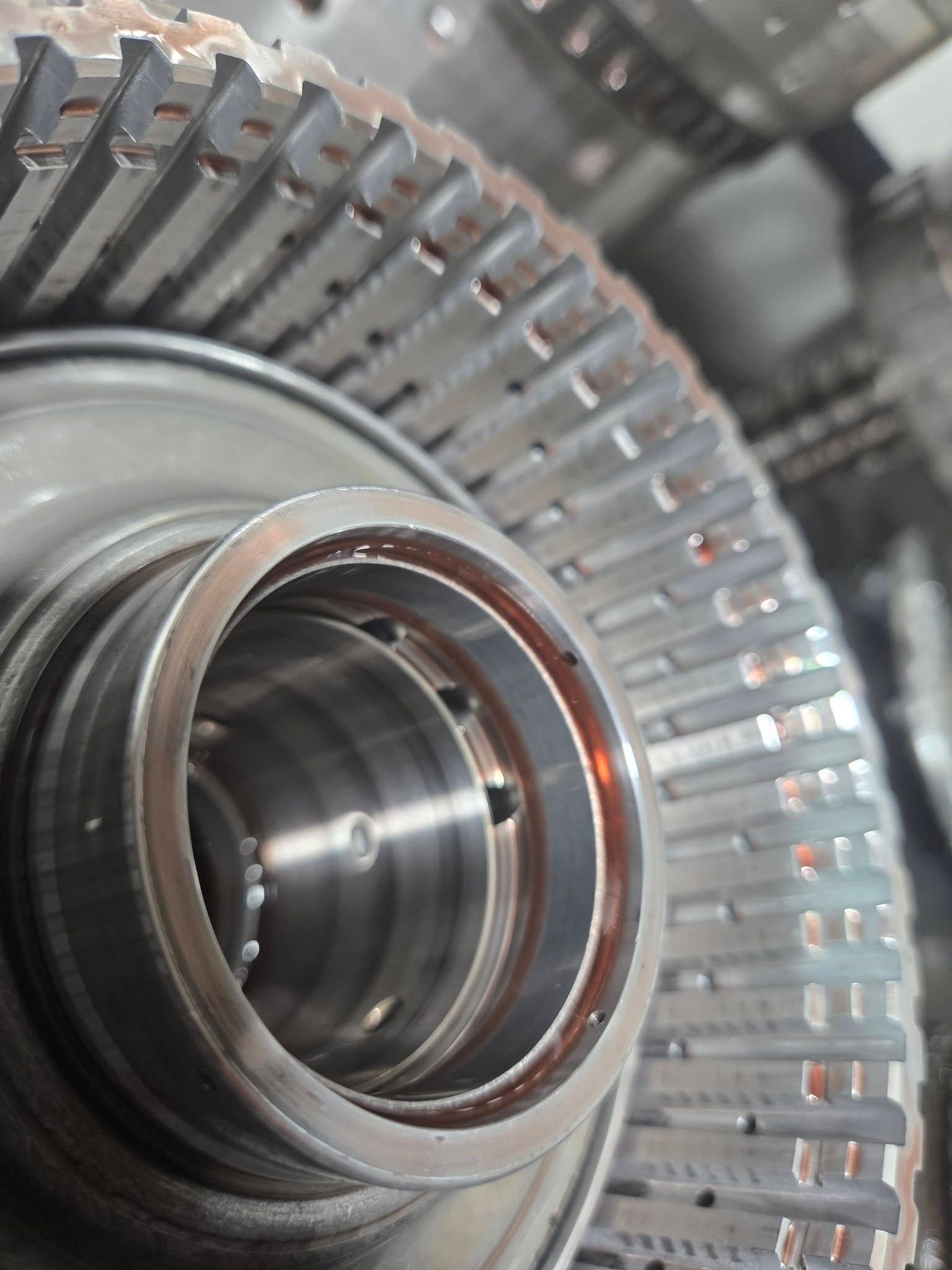Close-up of a metal gear or turbine wheel with a polished central bearing and blurred industrial background