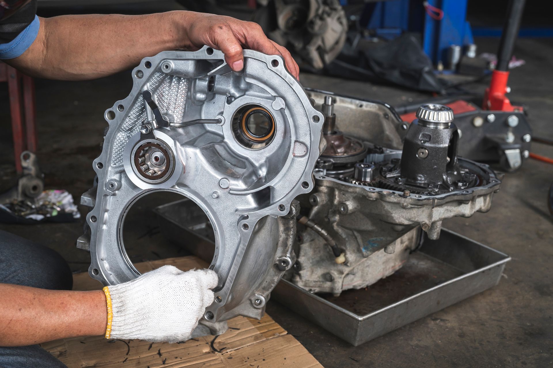 Mechanic holding a car transmission housing in a workshop during repair.