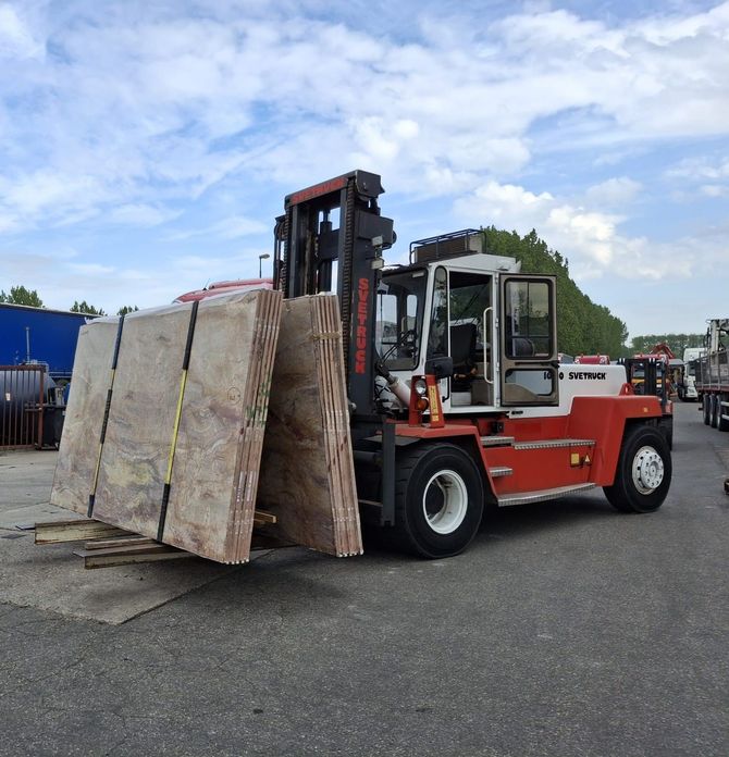 Een rode heftruck tilt grote houten kratten op in een grindterrein onder een gedeeltelijk bewolkte hemel.