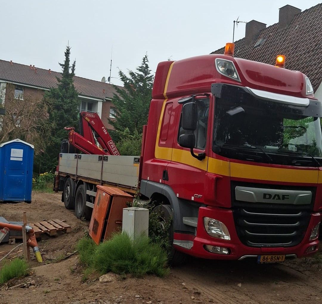 Een rode sleepwagen bergt een rode DAF-vrachtwagen van een modderige wegberm in de buurt van huizen.