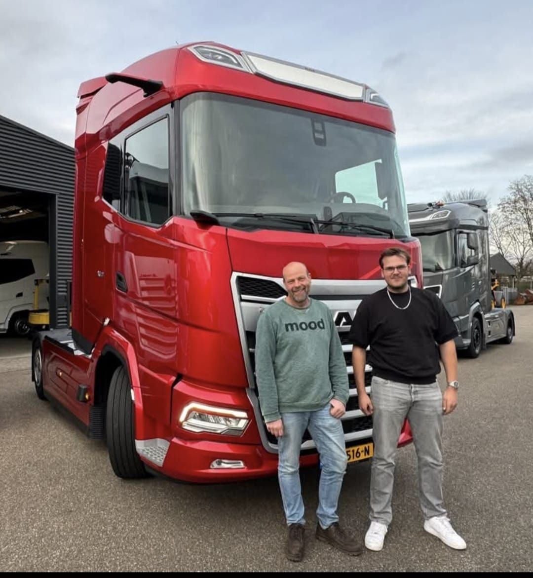 Twee mannen staan ​​naast een rode vrachtwagen op een parkeerplaats.