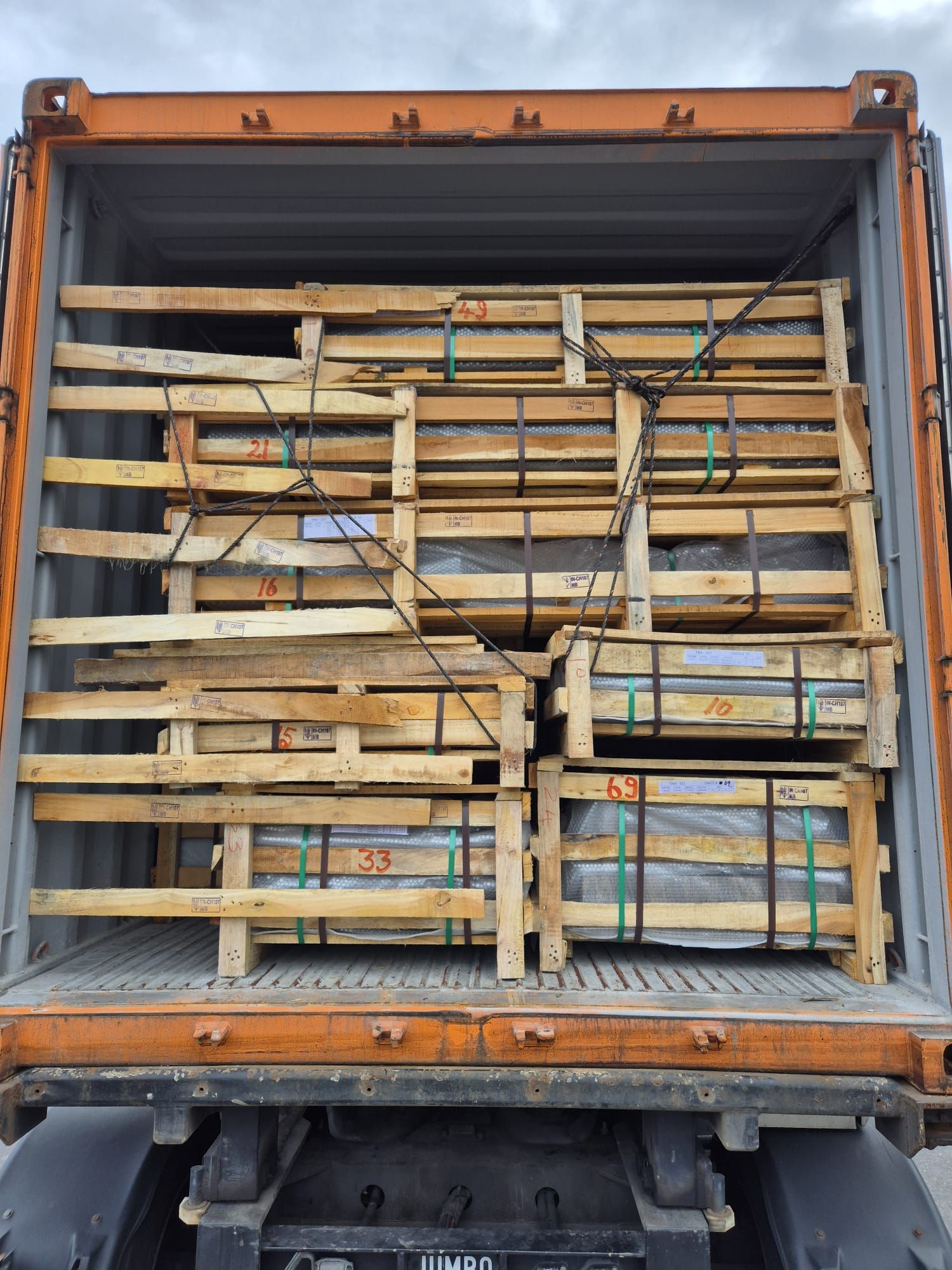Vrachtwagencontainer geladen met gestapelde houten kratten en bundels vastgezet met blauwe spanbanden.