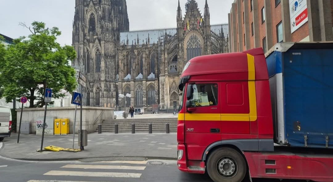 Rode vrachtwagen in een stadsstraat met een kathedraal op de achtergrond.