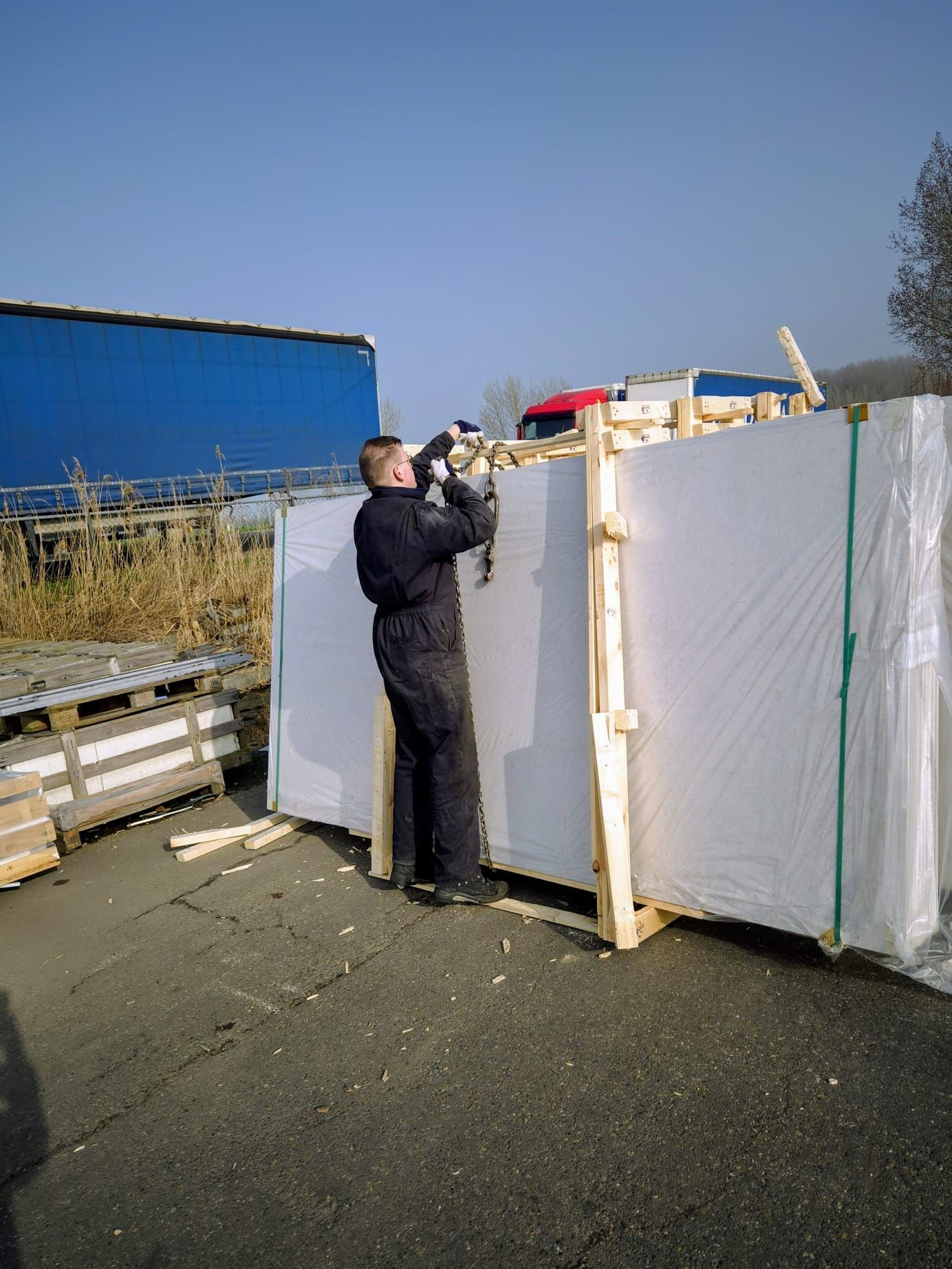 Een persoon bevestigt plastic zeilen aan een grote witte constructie in een zonnig industriegebied.