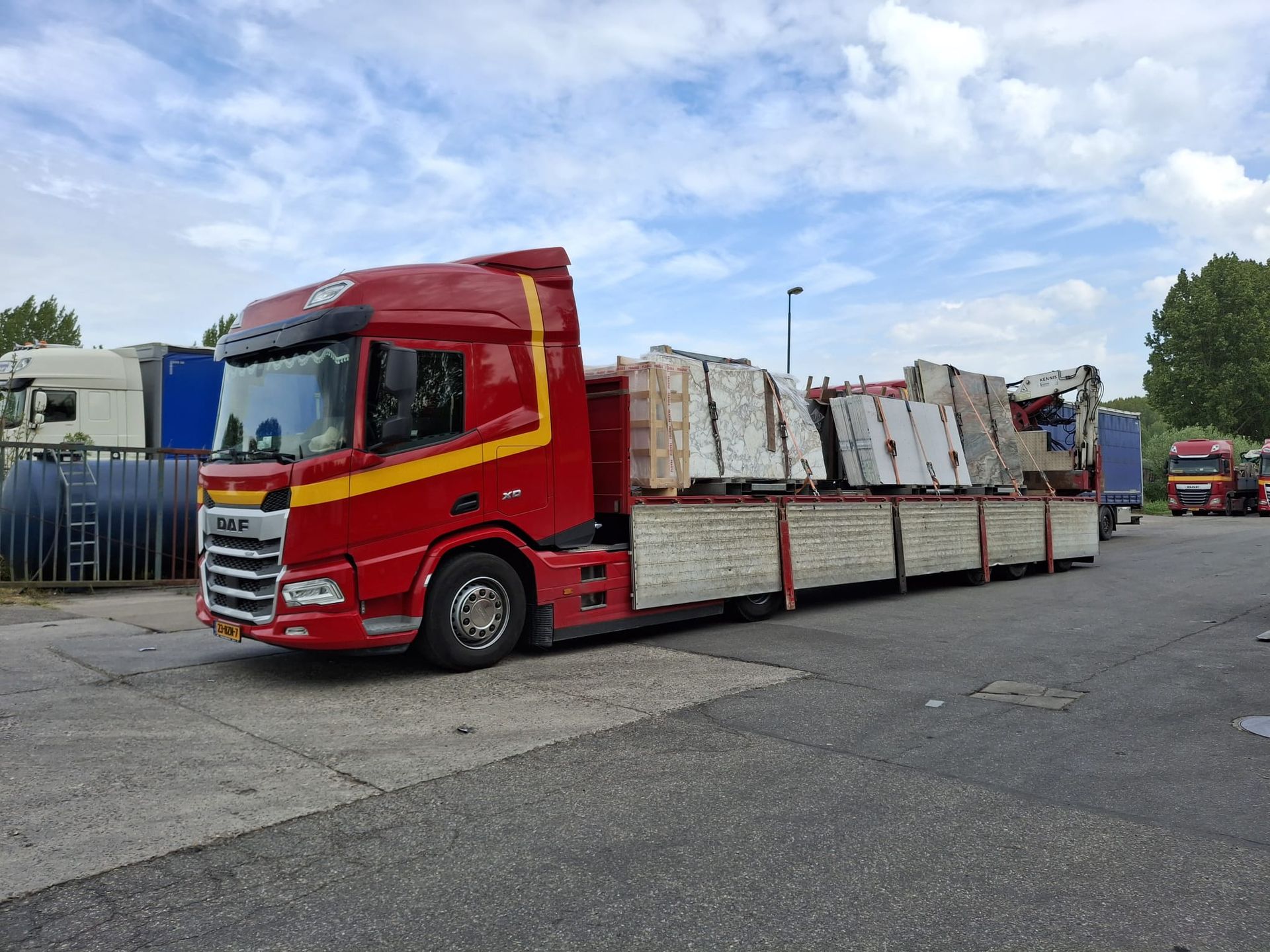 Rode vrachtwagen met open laadbak, beladen met gestapelde materialen, op een parkeerplaats onder een bewolkte hemel.