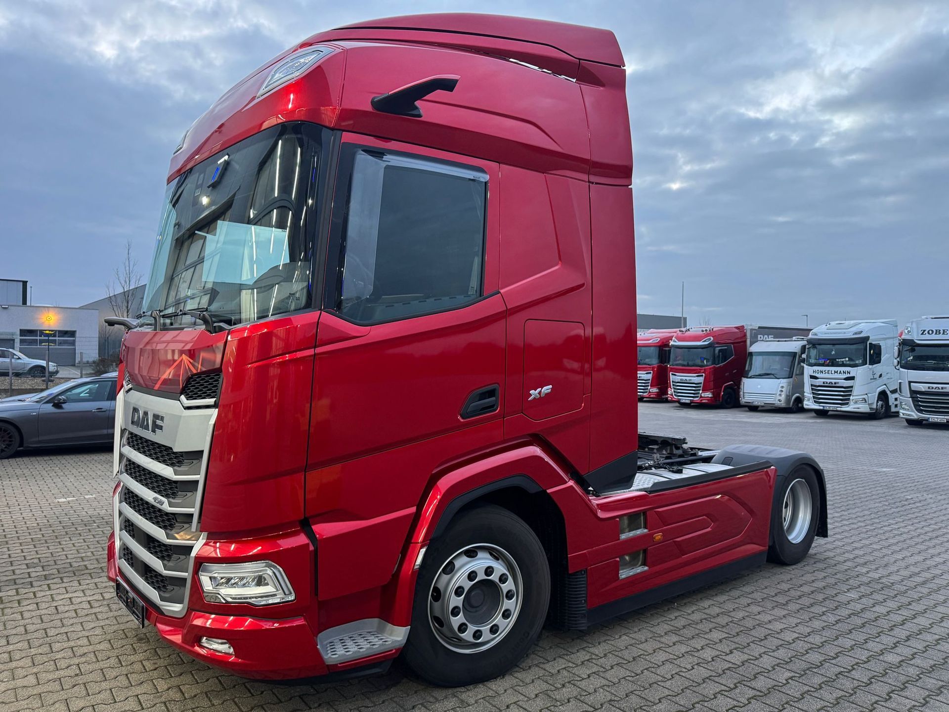 Rode vrachtwagen geparkeerd op een terrein onder een bewolkte hemel.