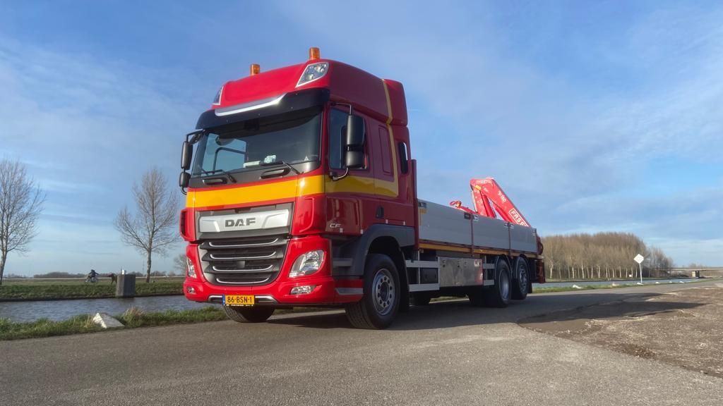 Een rood-gele vrachtwagen met open laadbak staat geparkeerd op een landweg onder een blauwe hemel.