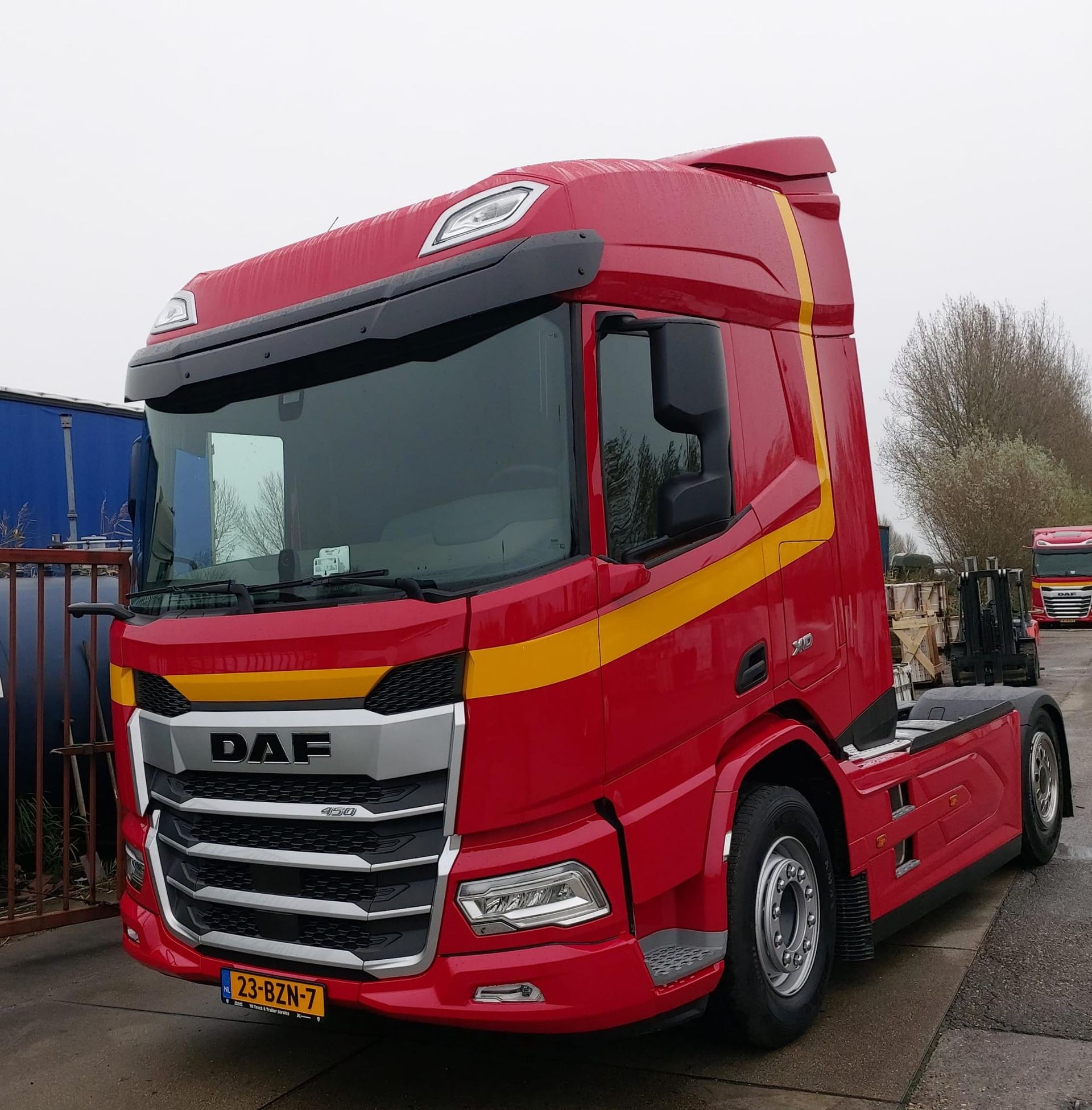 Rode DAF-vrachtwagencabine met gele streep, geparkeerd buiten in de buurt van zeecontainers.