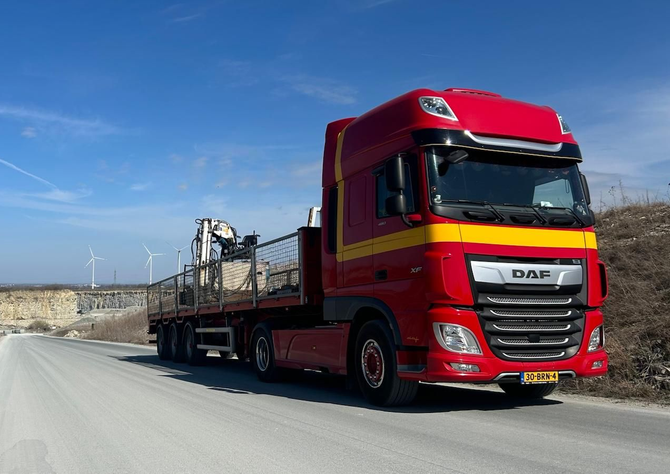 Een rode DAF-vrachtwagen met open laadbak rijdt over een snelweg onder een helderblauwe hemel.