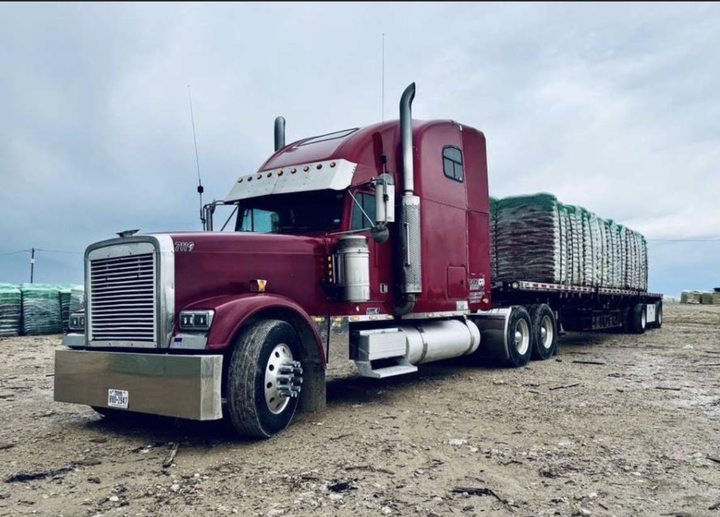 Black semi-truck hauling a white trailer on a roadside under a partly cloudy sky