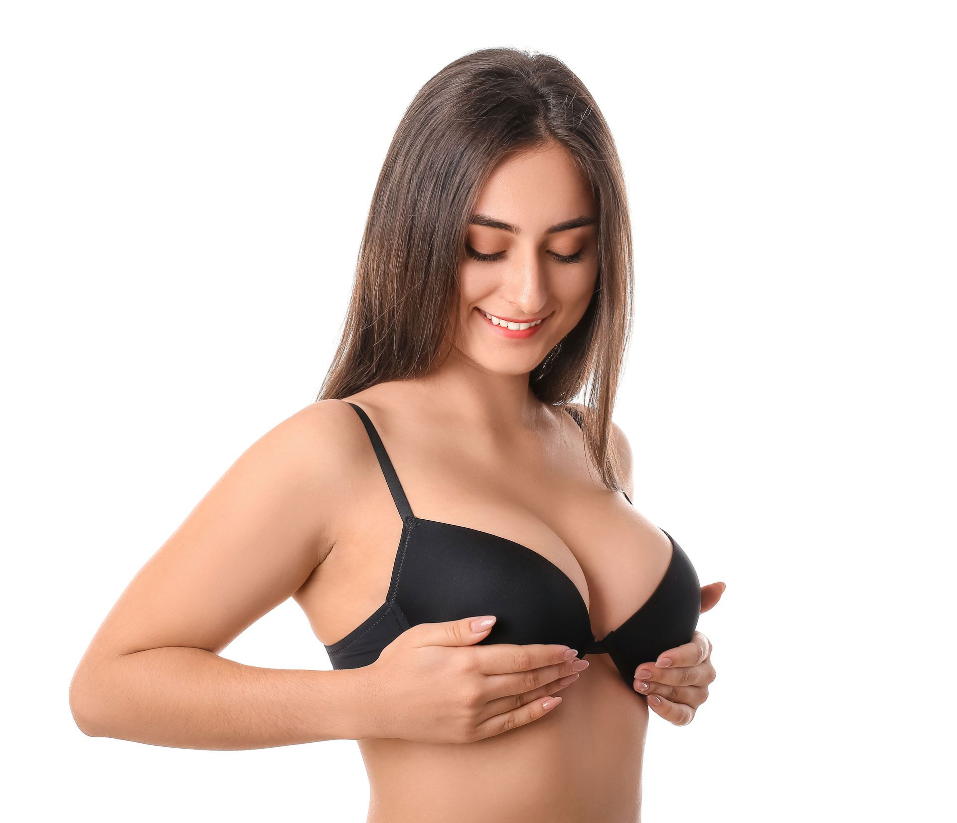 A smiling person wearing a black bra, holding their chest with both hands against a plain white background.