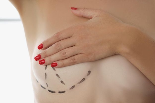 Woman measuring her chest with a tape measure, wearing a white bandeau top against a plain background