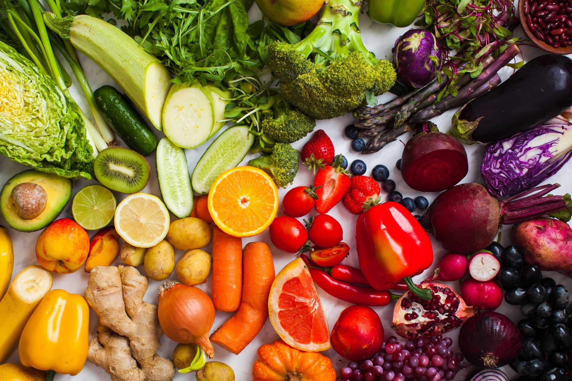 Disposizione di frutta e verdura colorata, tra cui broccoli, bacche, arance e barbabietole, su una superficie bianca.