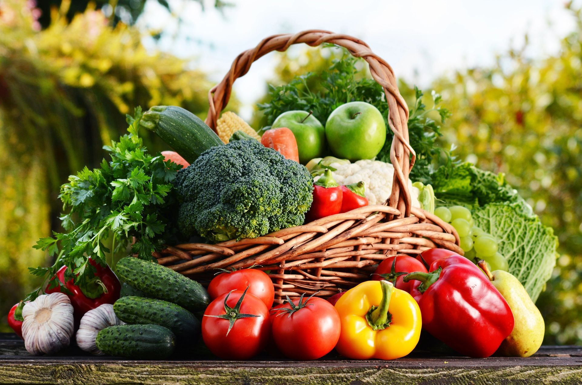 Cestino traboccante di verdure fresche e colorate: pomodori, peperoni, broccoli, cetrioli, mele e molto altro.