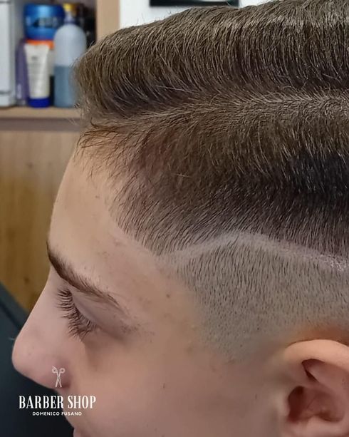 Taglio di capelli di profilo con lati sfumati e parte superiore acconciata, in una barberia.