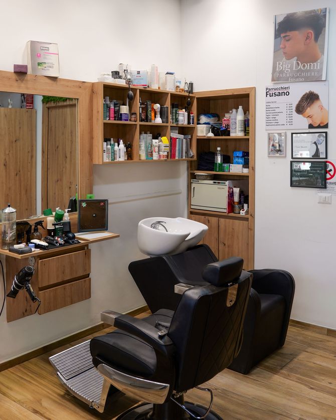 Interni moderni di un salone da parrucchiere con poltrone per lo styling, specchi e postazioni in legno accanto a grandi finestre.