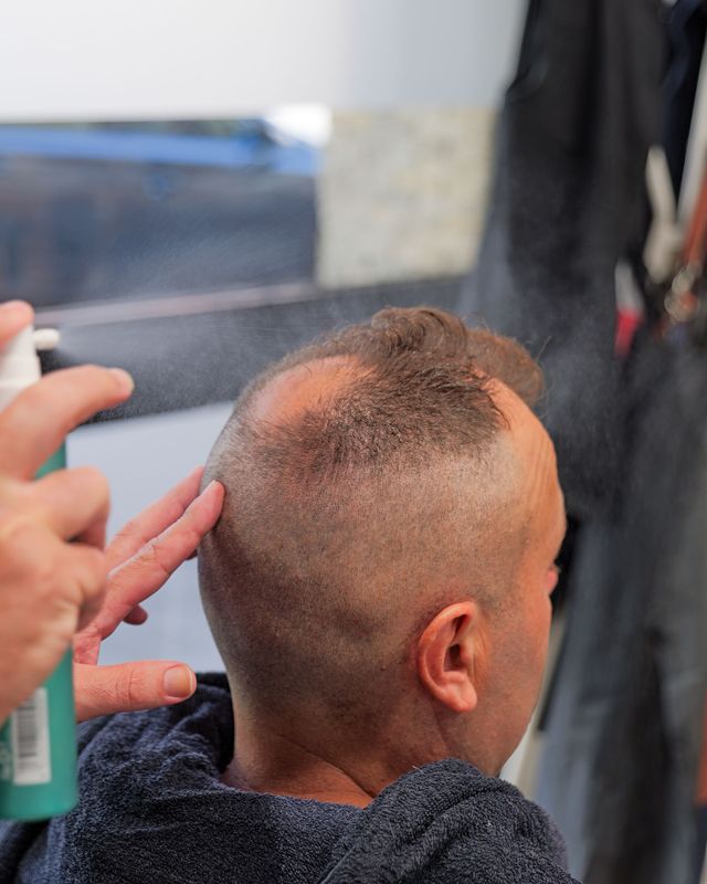 Parrucchiere che acconcia i capelli di una cliente in un salone, utilizzando tosatrici e pettine.