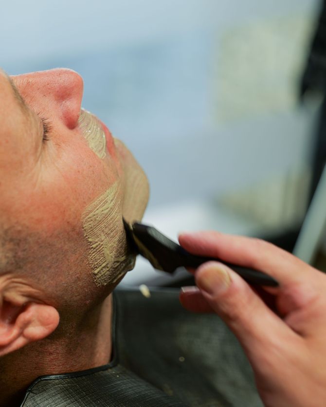 Un barbiere taglia la barba a un uomo seduto sulla poltrona di un negozio di barbiere.