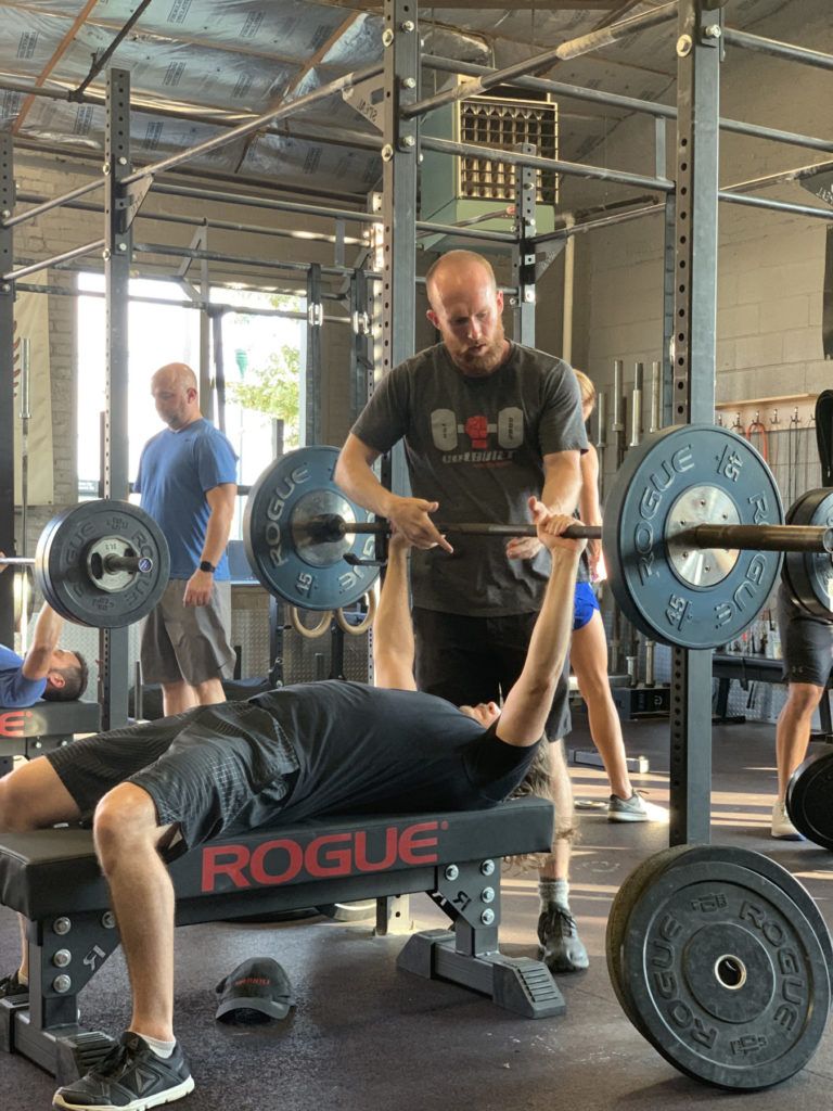 A man is lifting a barbell on a bench in a gym.