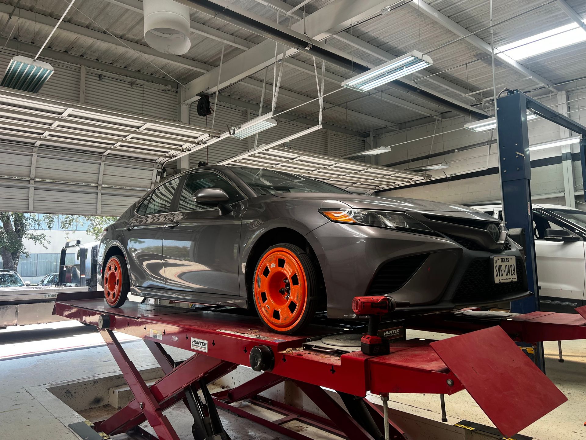 Dark gray sports car with orange wheels on a red lift in an auto shop