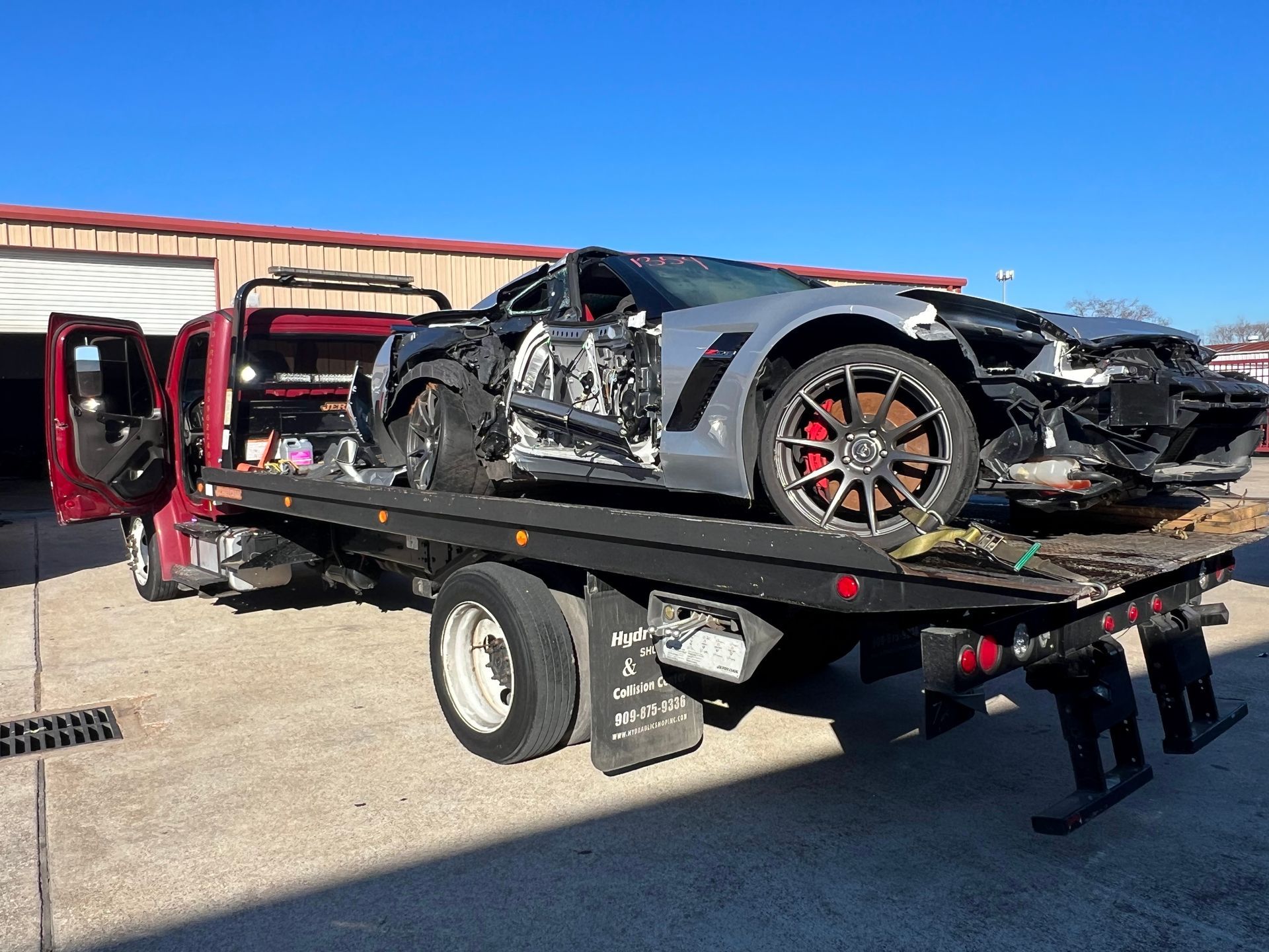 Damaged black sports car on a tow truck with its driver door open in a parking lot