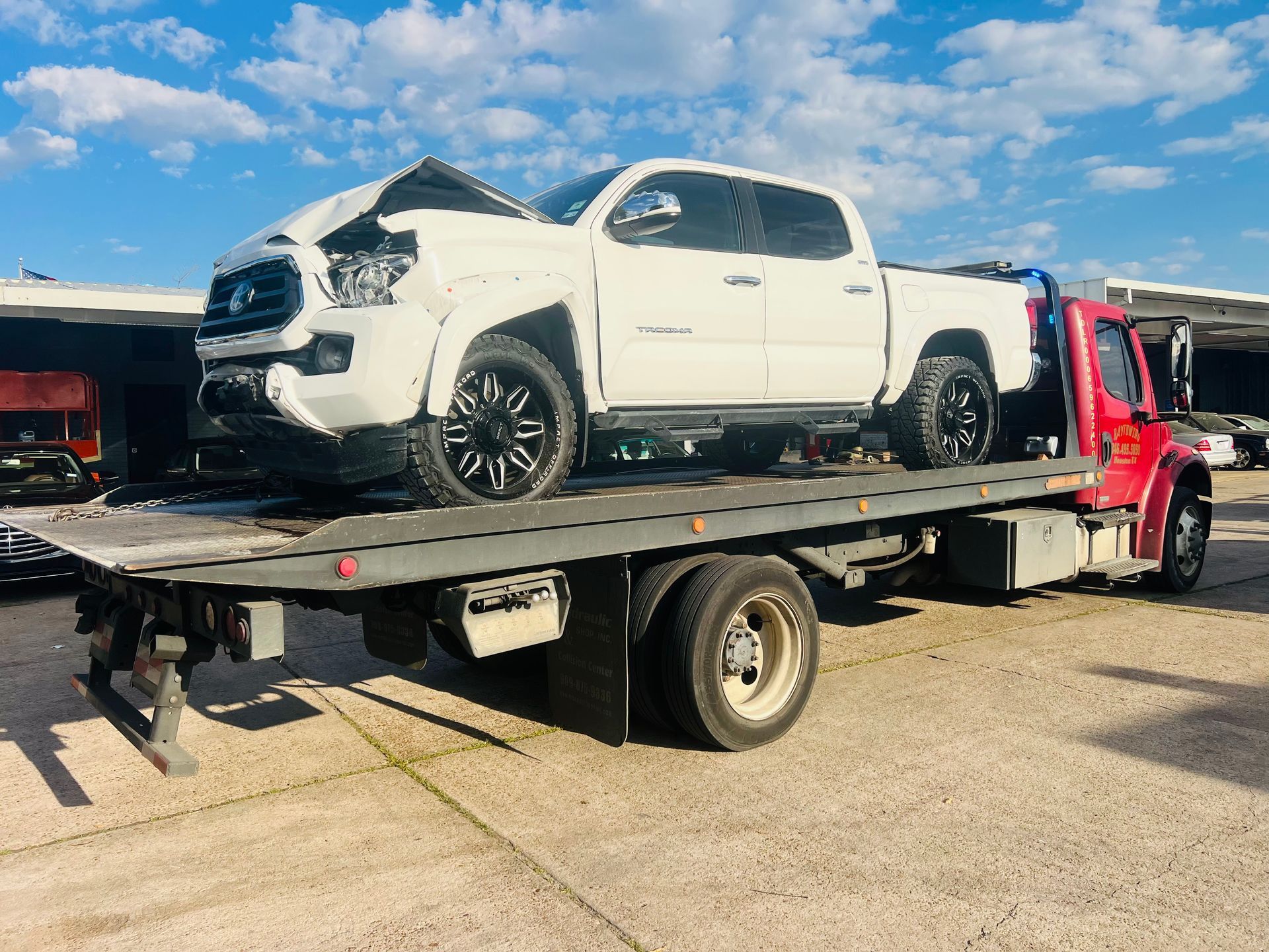 White pickup truck loaded on a red flatbed tow truck under a blue sky