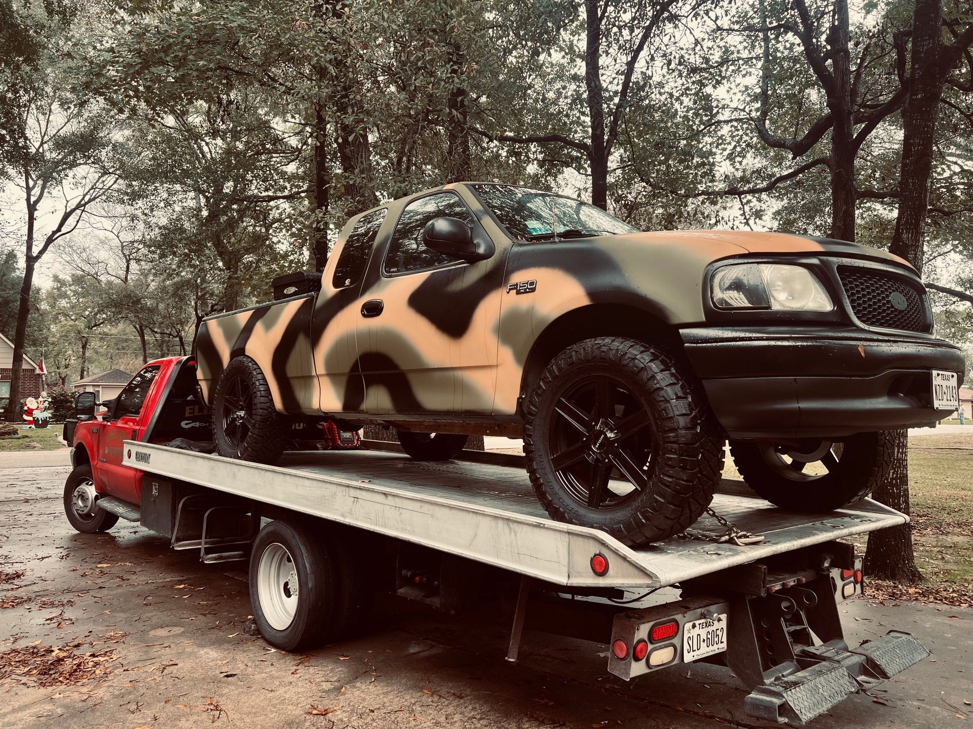 Camouflage-painted SUV strapped on a flatbed trailer in a wooded park area
