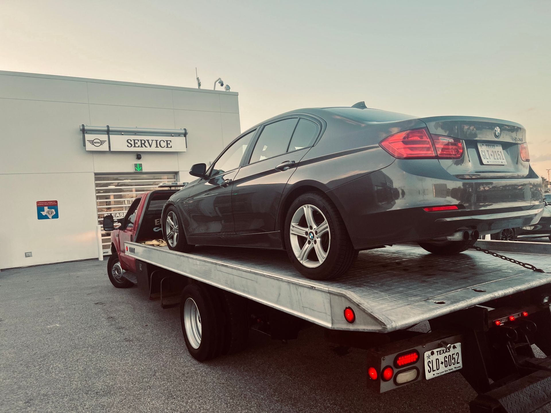 Dark sedan on a tow truck bed outside a service garage