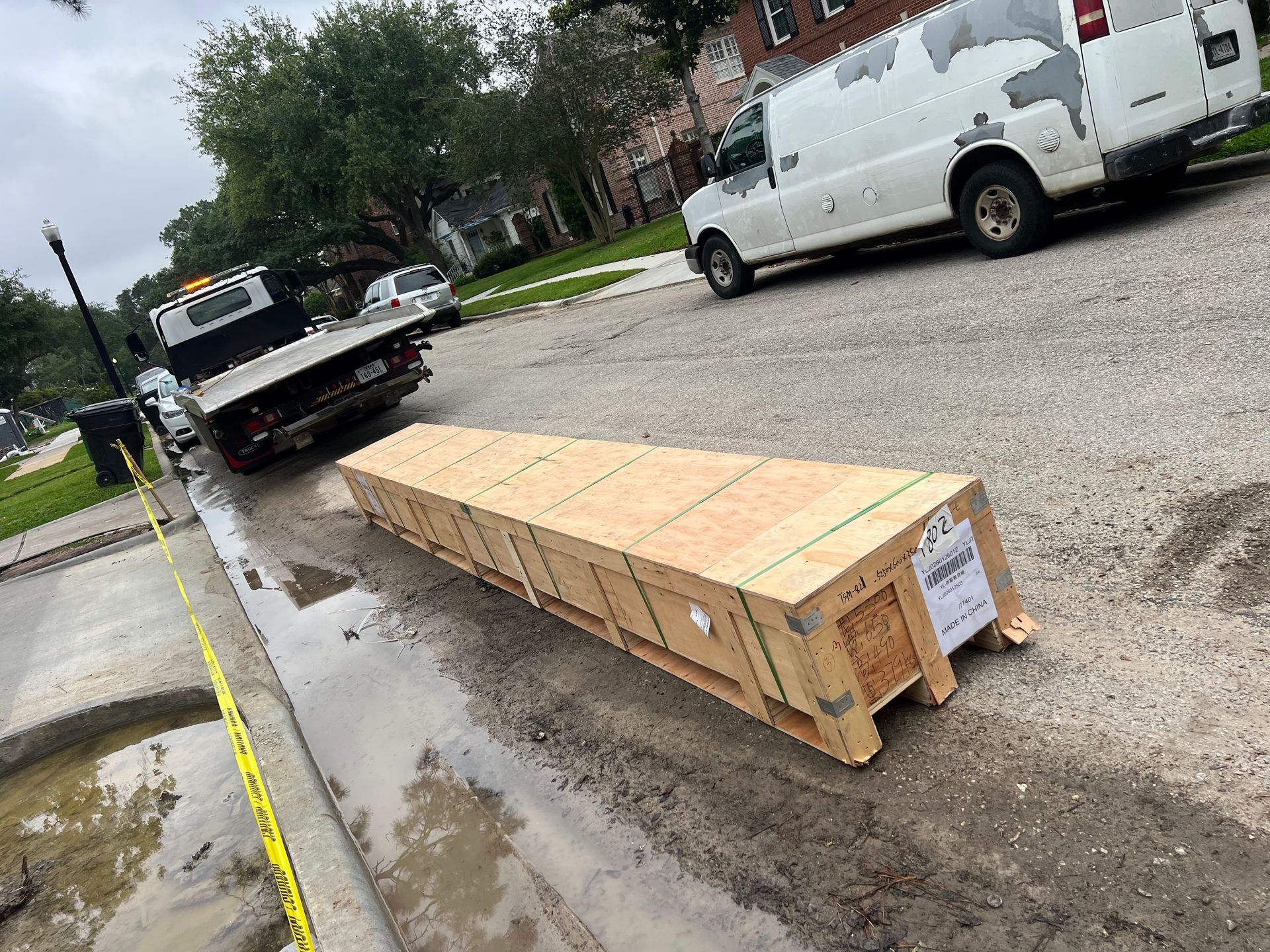 Long wooden crate on wet street beside a tow truck and white van