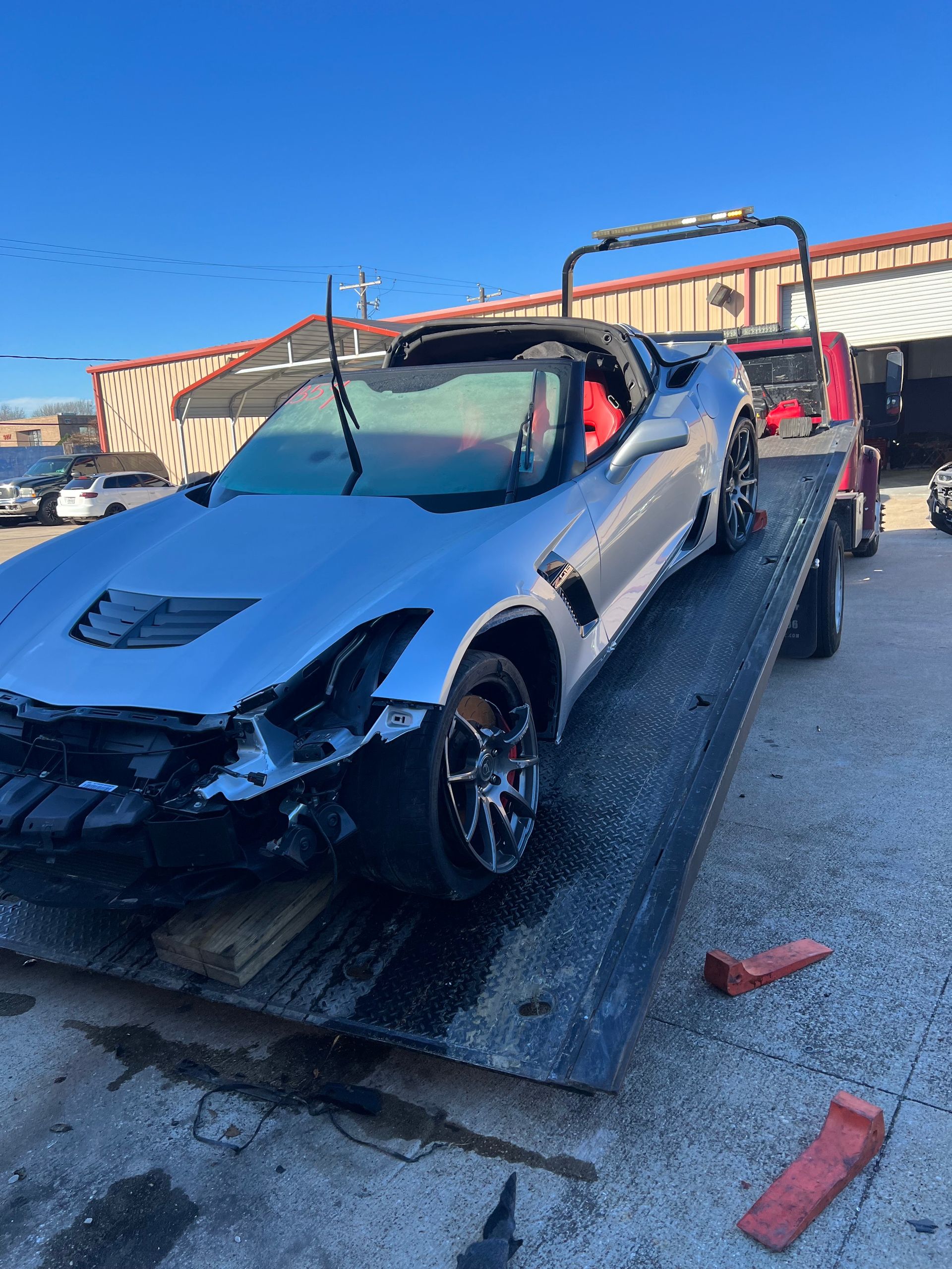Damaged silver sports car loaded on a tow truck in a parking lot