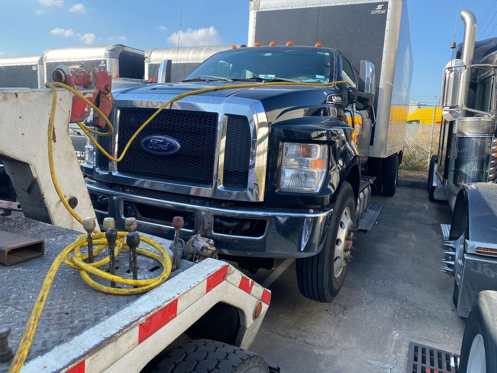 Black Ford tow truck hooked to cables in a lot between other trucks and a trailer