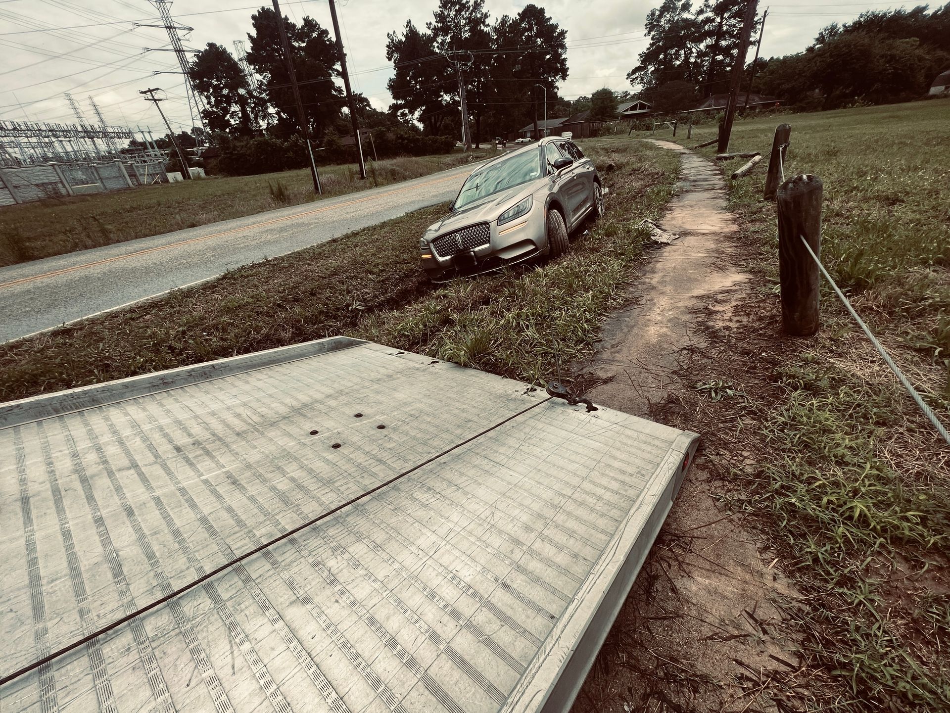 Car overturned in roadside ditch beside a rural road, with a fallen metal gate in the foreground.
