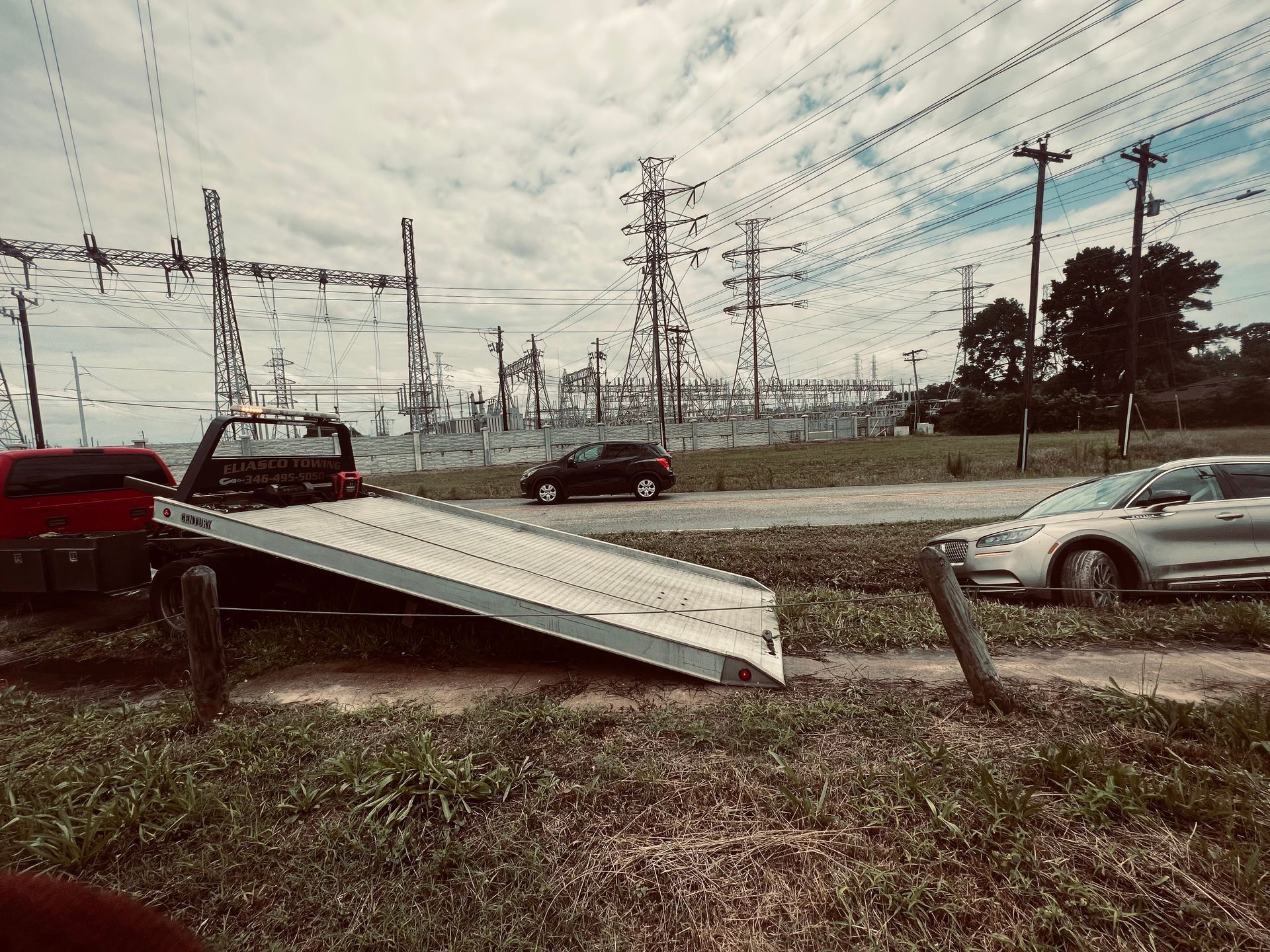 Car crashed on a tilted utility pole in a grassy rail yard, with trains and power lines in the background