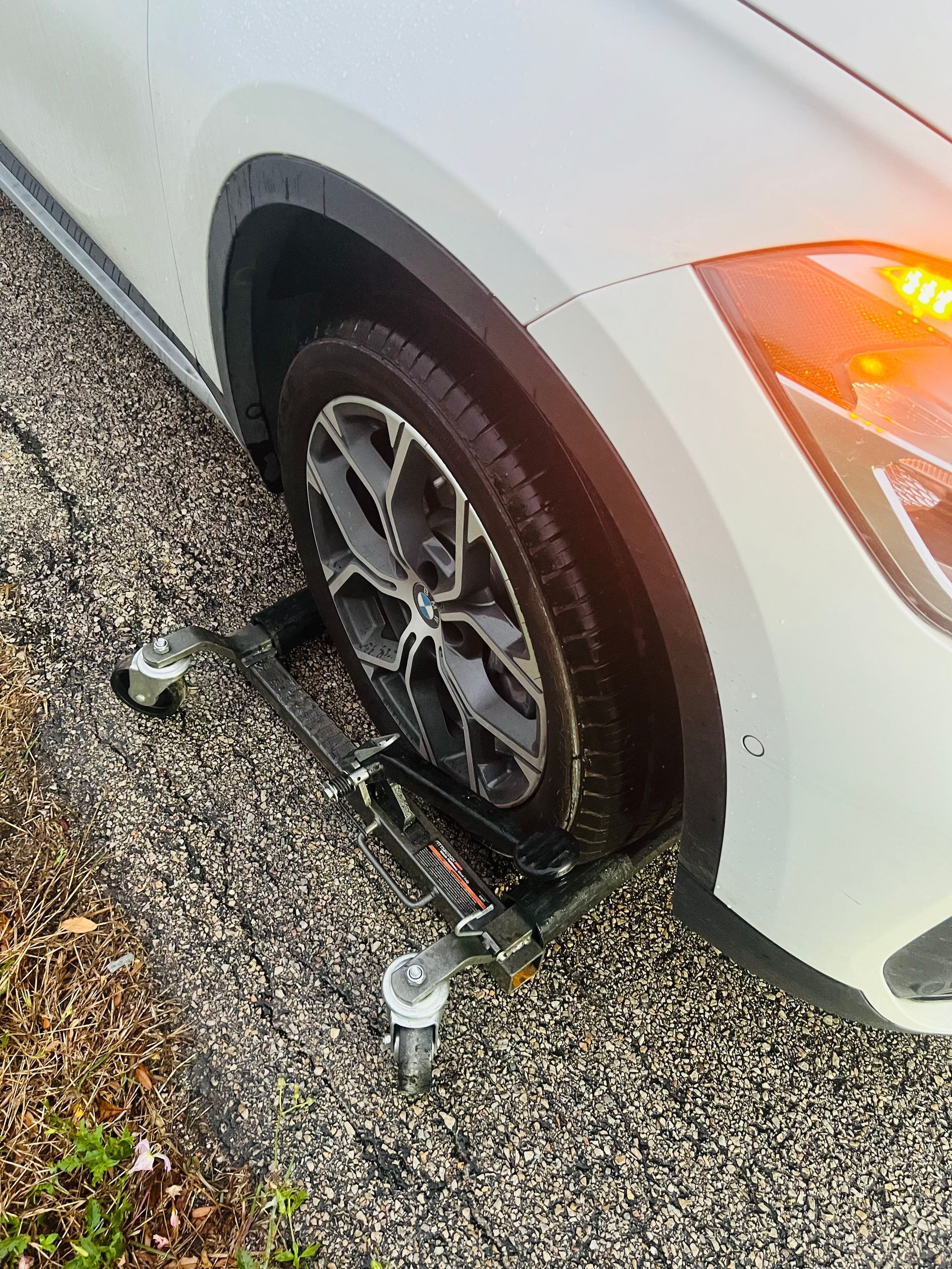 White car with a front wheel clamped by a boot on a wet gravel road