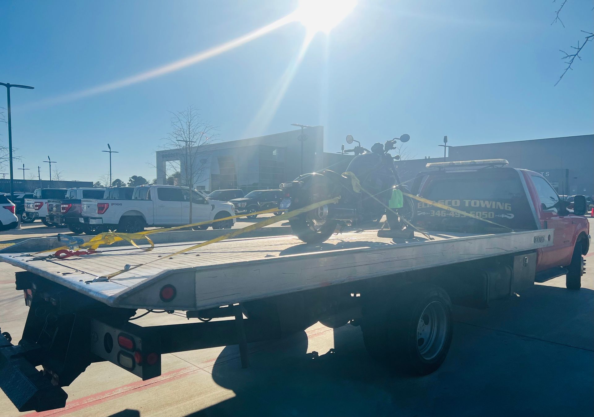 Tow truck hauling a flatbed trailer in a sunny parking lot