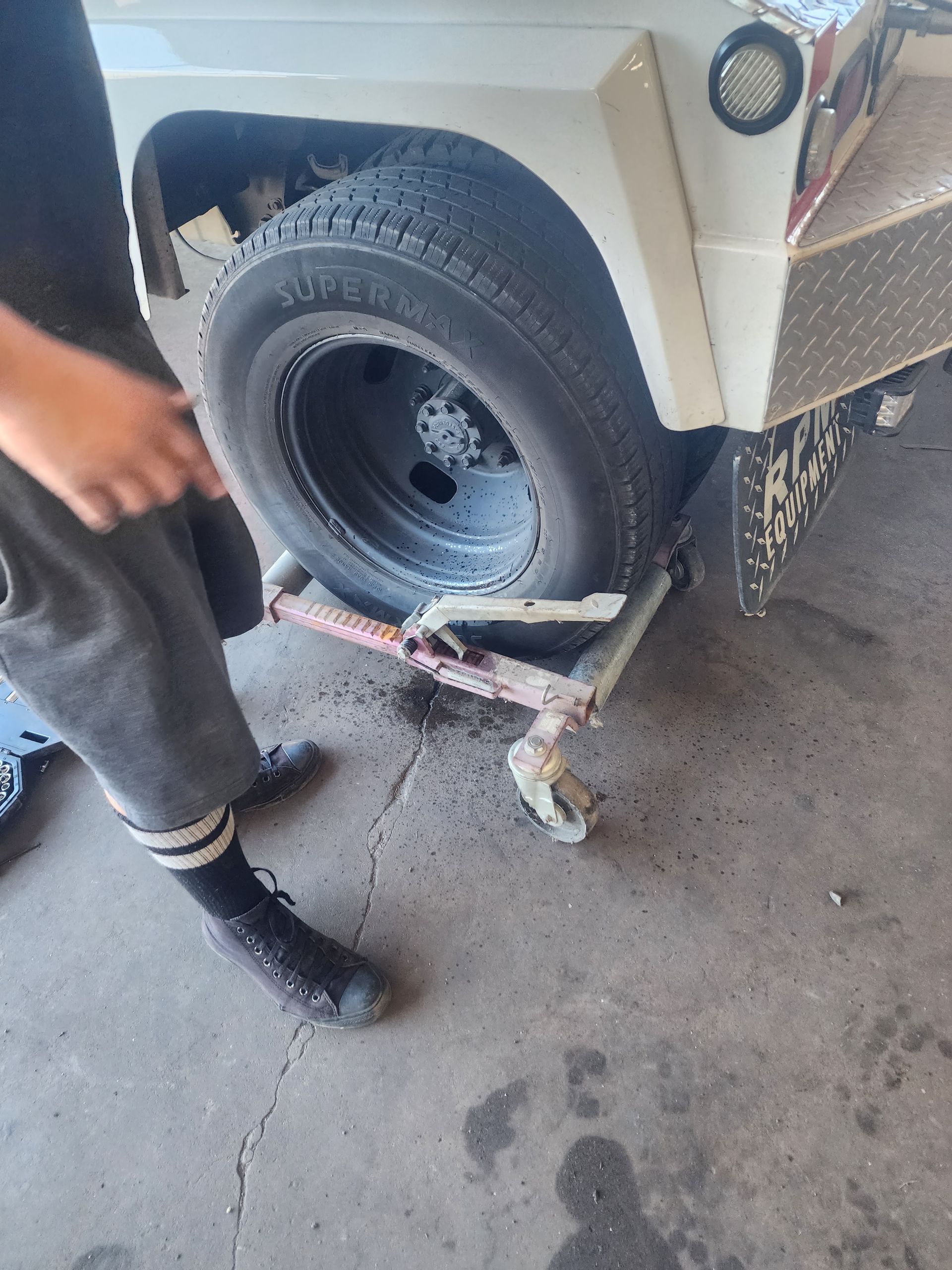 Person using a jack to lift a white vehicle’s rear tire in a garage.