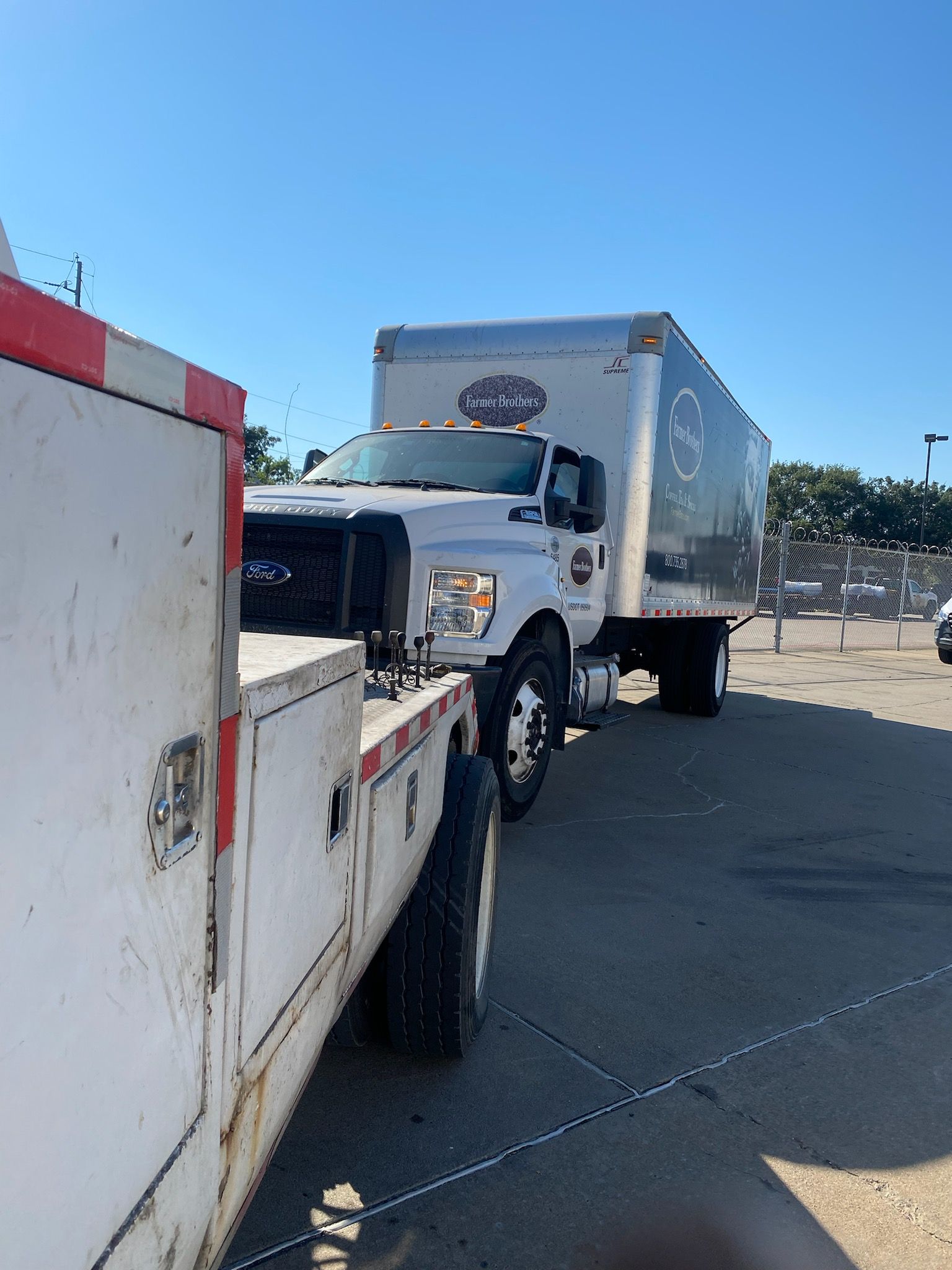 Tow truck pulling a white box truck in a sunny parking lot