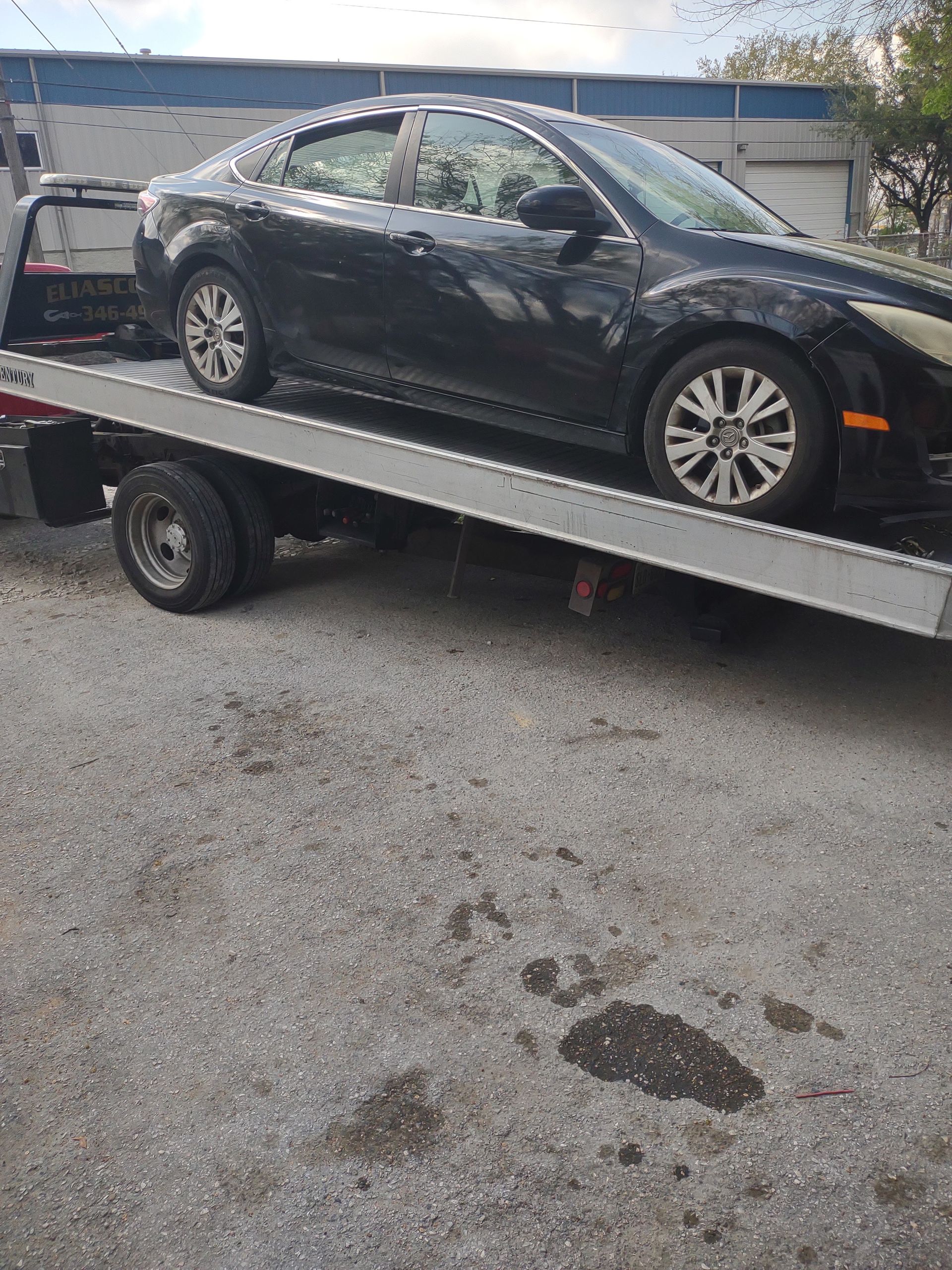 Black sedan loaded on a flatbed tow truck in a parking lot