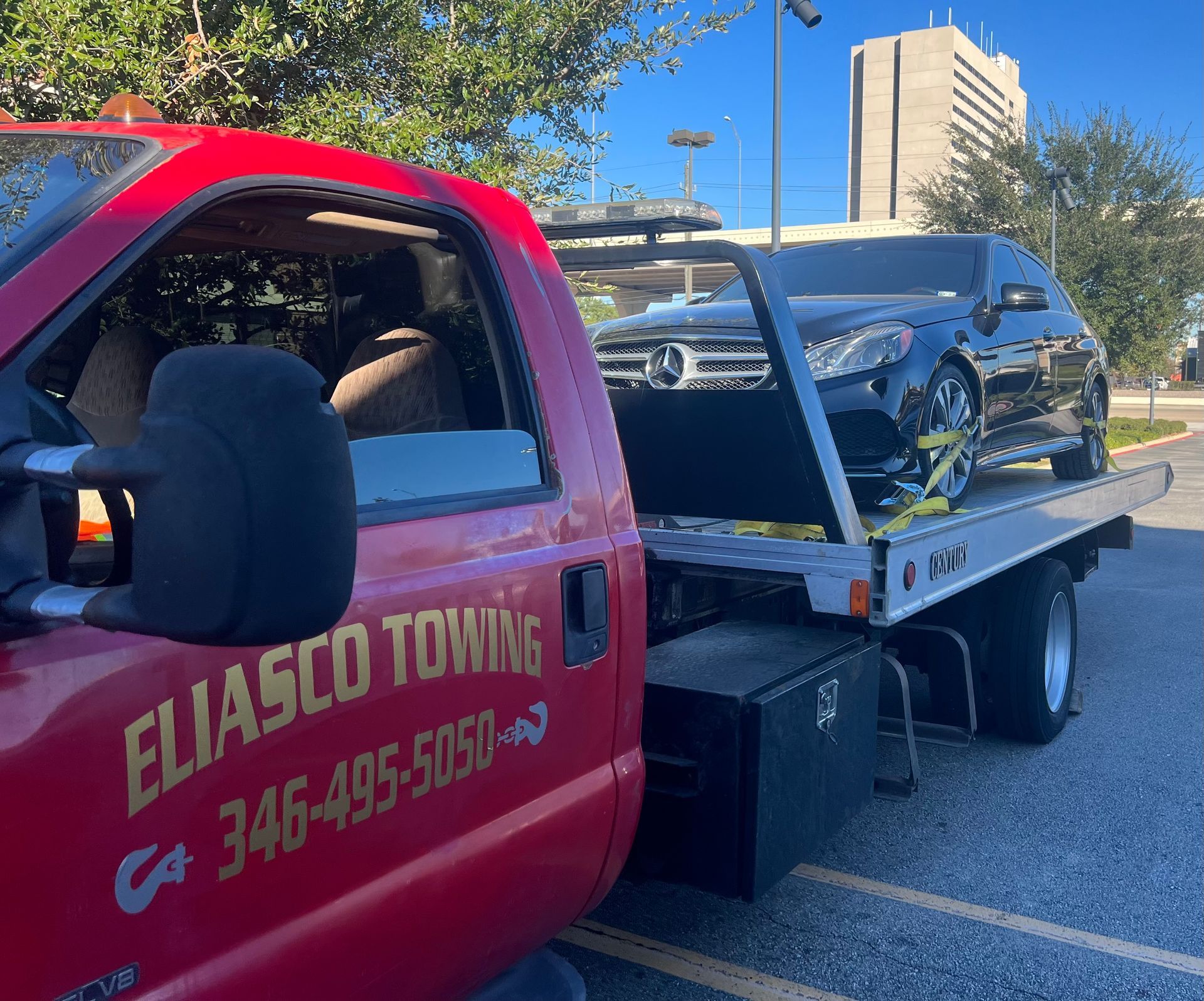Red tow truck hauling a black SUV on a flatbed in daylight.
