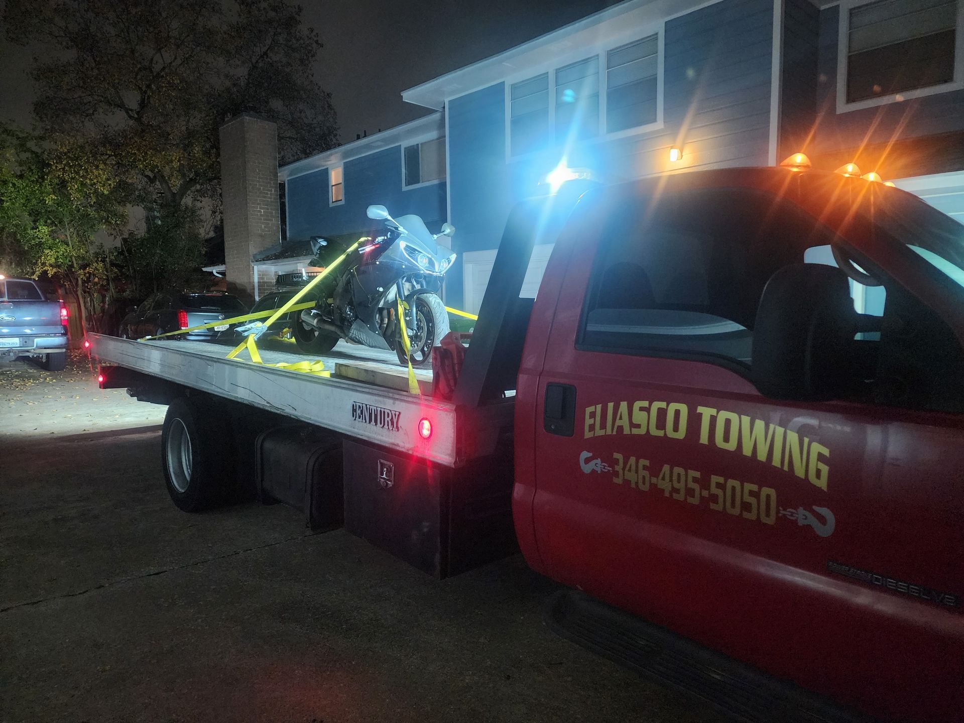 Tow truck with flashing lights towing a car at night in a residential area
