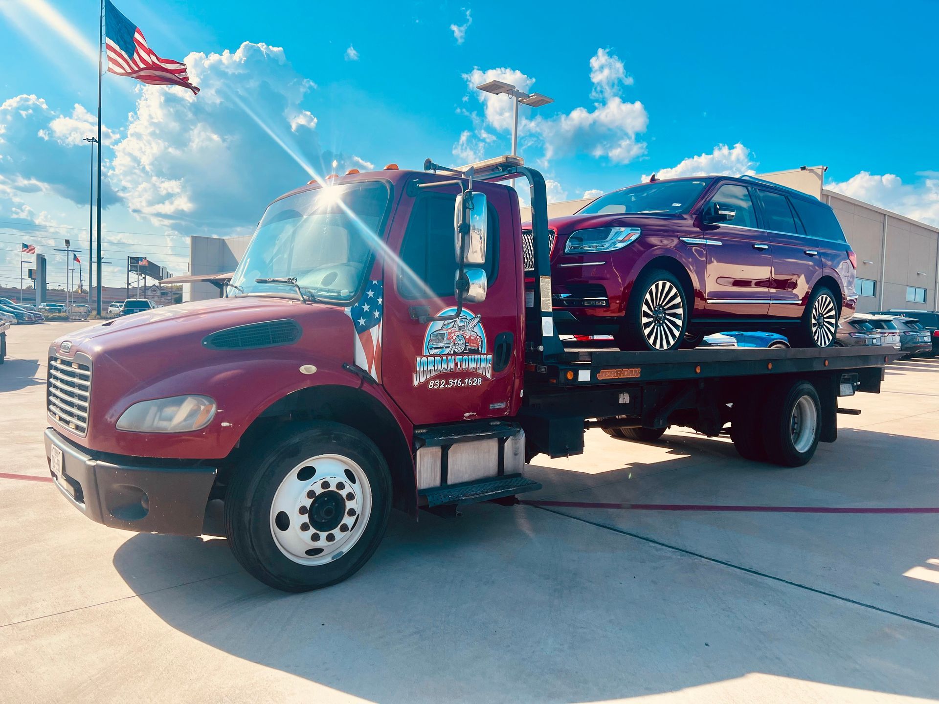 Red tow truck hauling a maroon SUV on a sunny roadside.