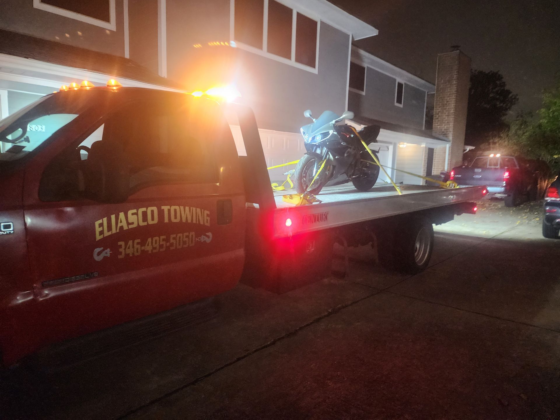 Tow truck loading a motorcycle on a city street at night with flashing amber lights