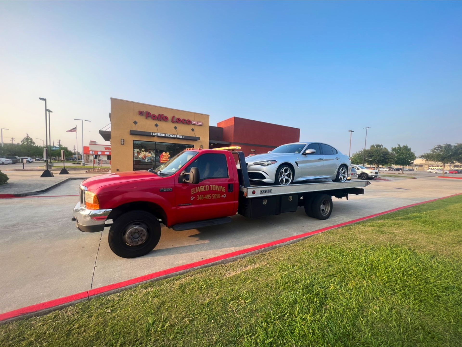 Red tow truck carrying a silver car outside a parking lot